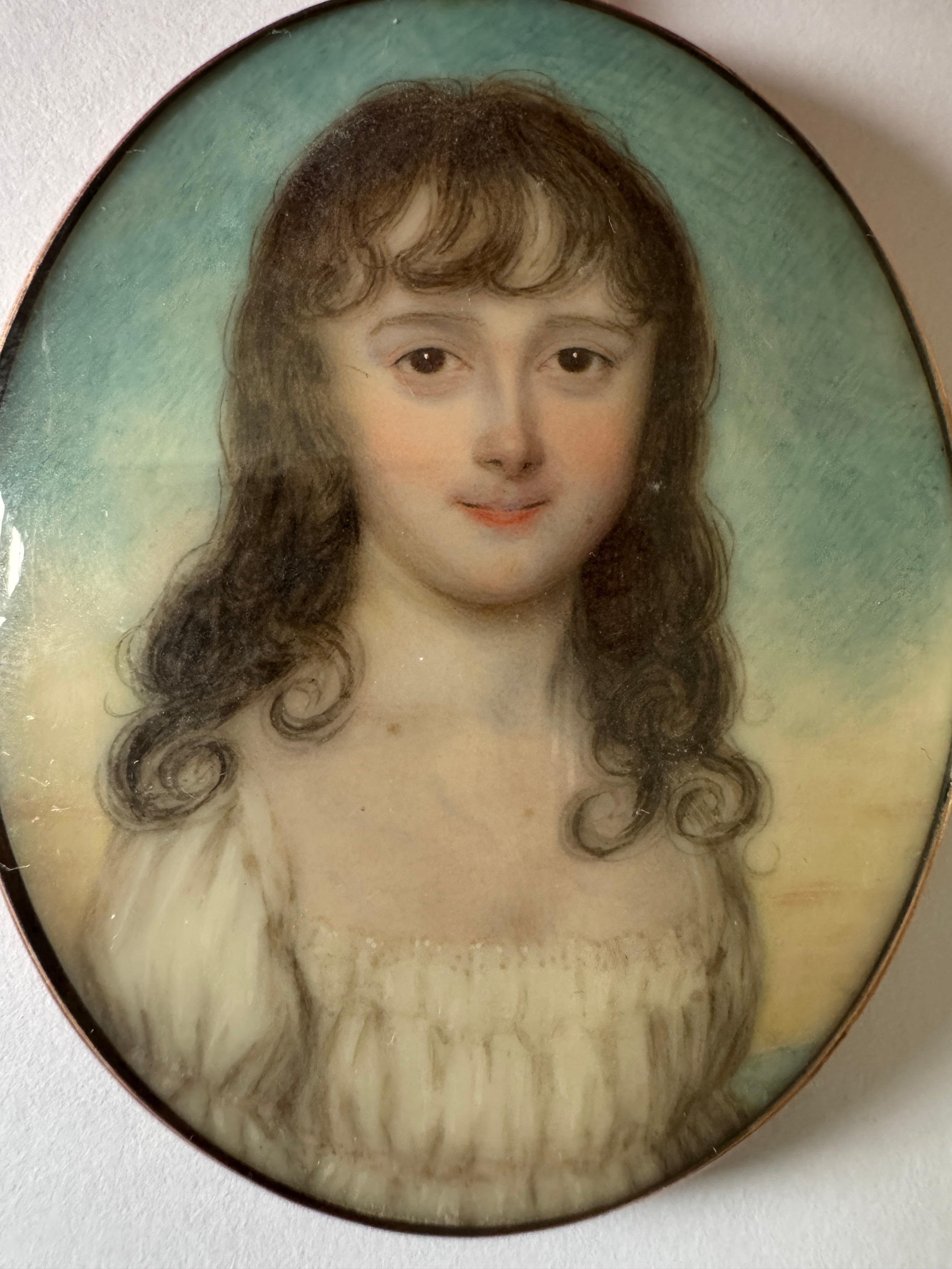 18th Century Portrait Miniature - Style of William Wood (1768 -1809) , A young girl, bust length, with long curling brown hair and wearing a white dress, sky background. Watercolour. Oval 6.5cm. In a gold frame with a guilloche back.

UK Ivory