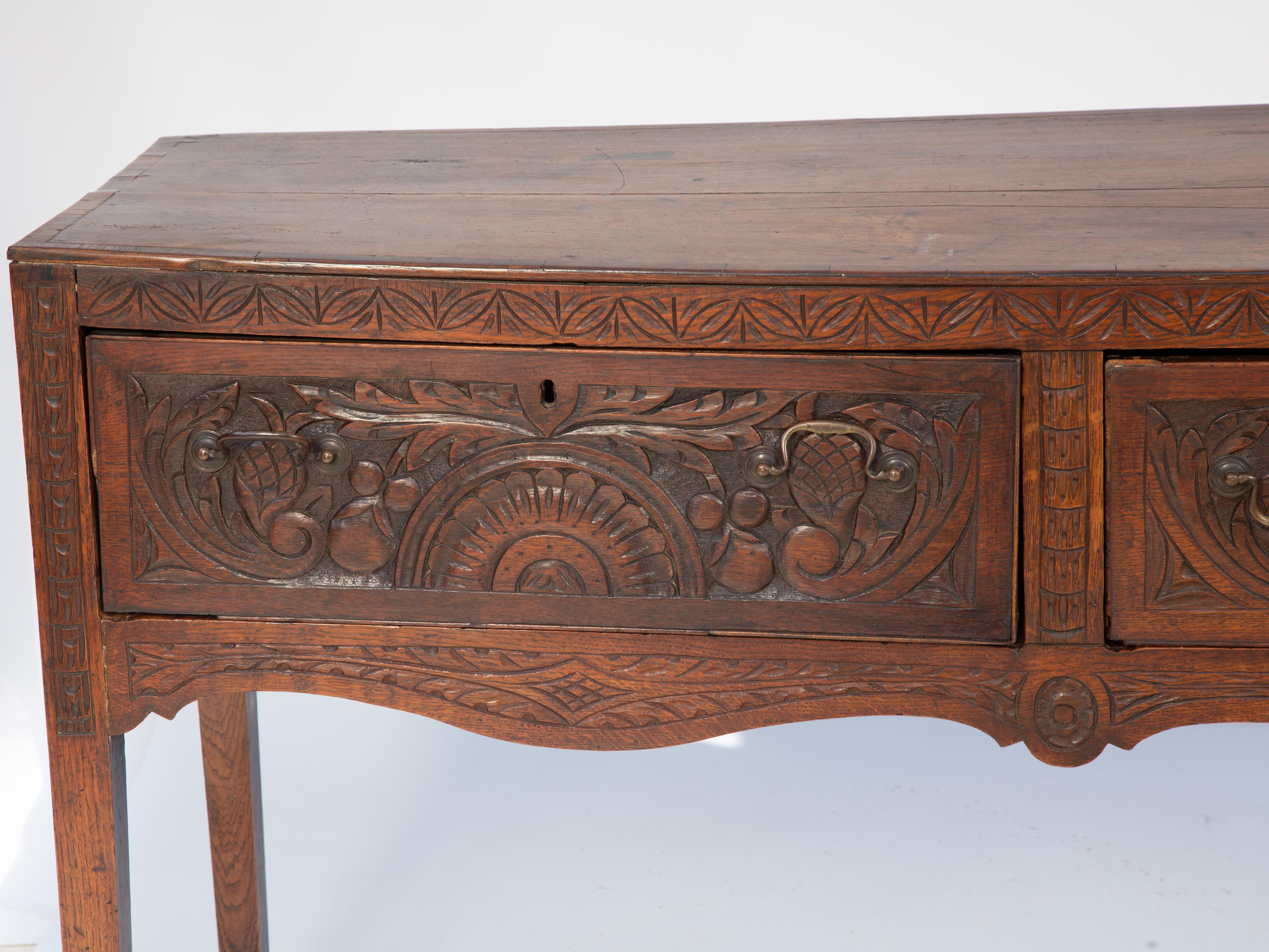 Antique serving table console, of elmwood, having a rectangular top over triple frieze drawers, each hand carved with palmettes flanked by scrollwork, its front decorated by incarved crosshathing, on foliate-carved serpentine stretcher, raised on