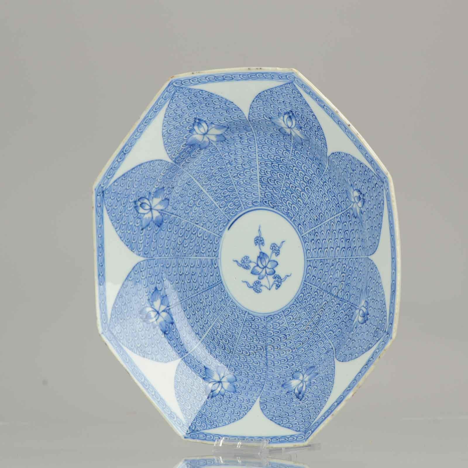 Blauer und weißer, achteckiger Exportteller, in der Mitte verziert mit einer stilisierten Lotusblumenpracht, umrahmt von Lotusblütenblättern, die Lotusblumen auf einem Rollwerkgrund einschließen.

Dieses Muster wurde in chinesischem