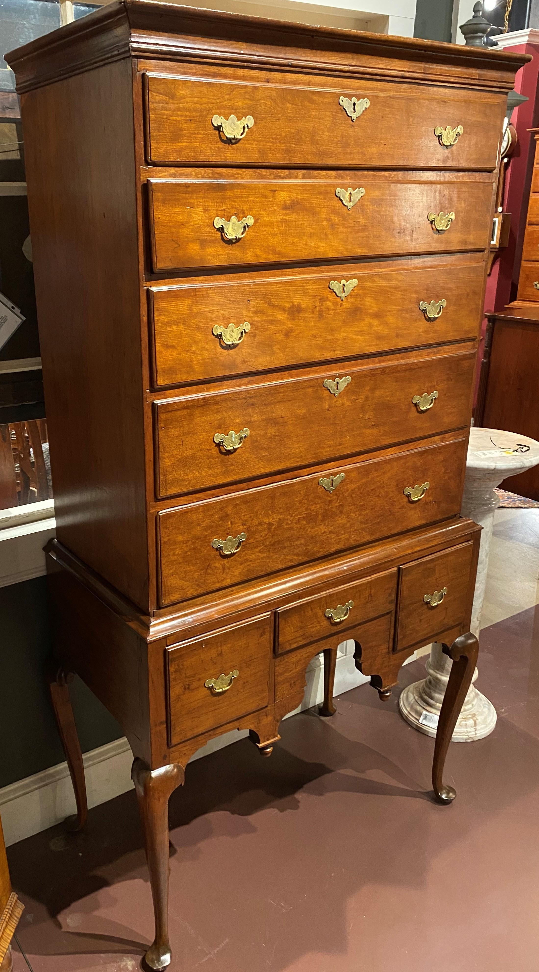 A fine Queen Anne two part highboy with a molded cornice surmounting an upper case with five graduated drawers over an associated lower case with three fitted drawers, all with early engraved batwing brasses with cotter pins. The skirt is nicely