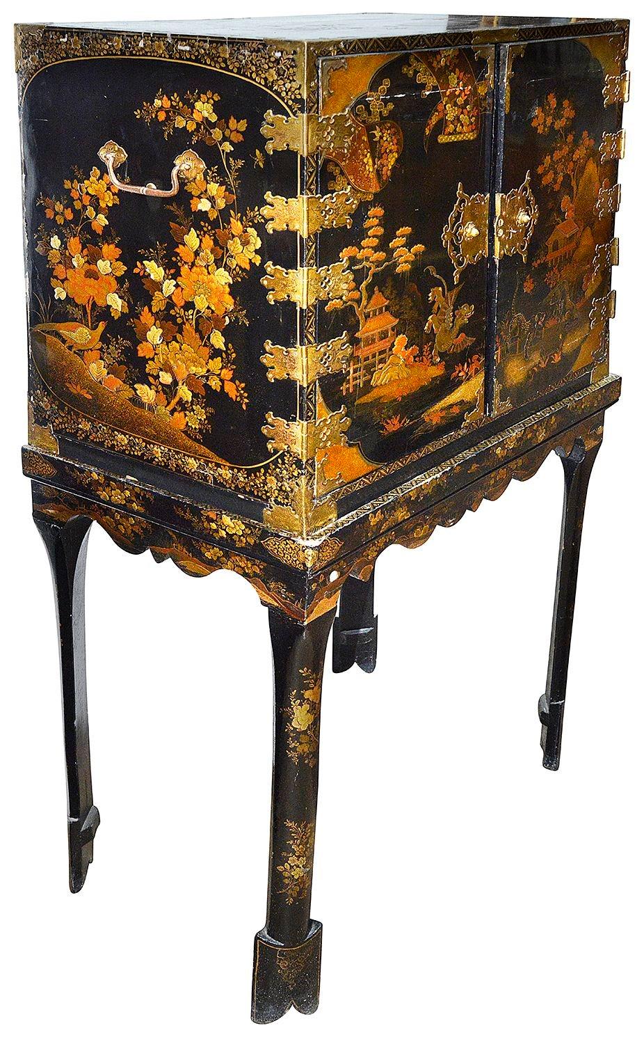 Armario lacado de época Queen Anne, bellamente decorado, sobre peana. Con bisagras y placas de cierre de latón calado y perforado. Las puertas presentan escenas de chinoiserie y se abren para revelar diez cajones empotrados, cada uno de ellos con