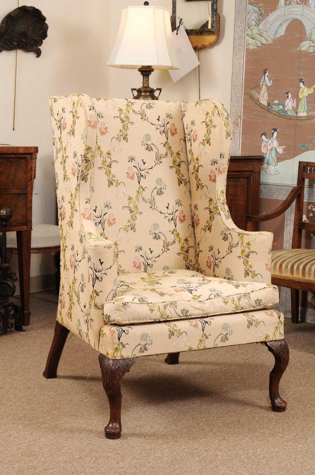 The New England Queen Anne style wing chair with rectangular back flanked by shaped ears leading out to scrolled arms. The wing chairs in need point upholstery with loose cushion seat and raised on carved cabriole legs terminating in pad feet.
