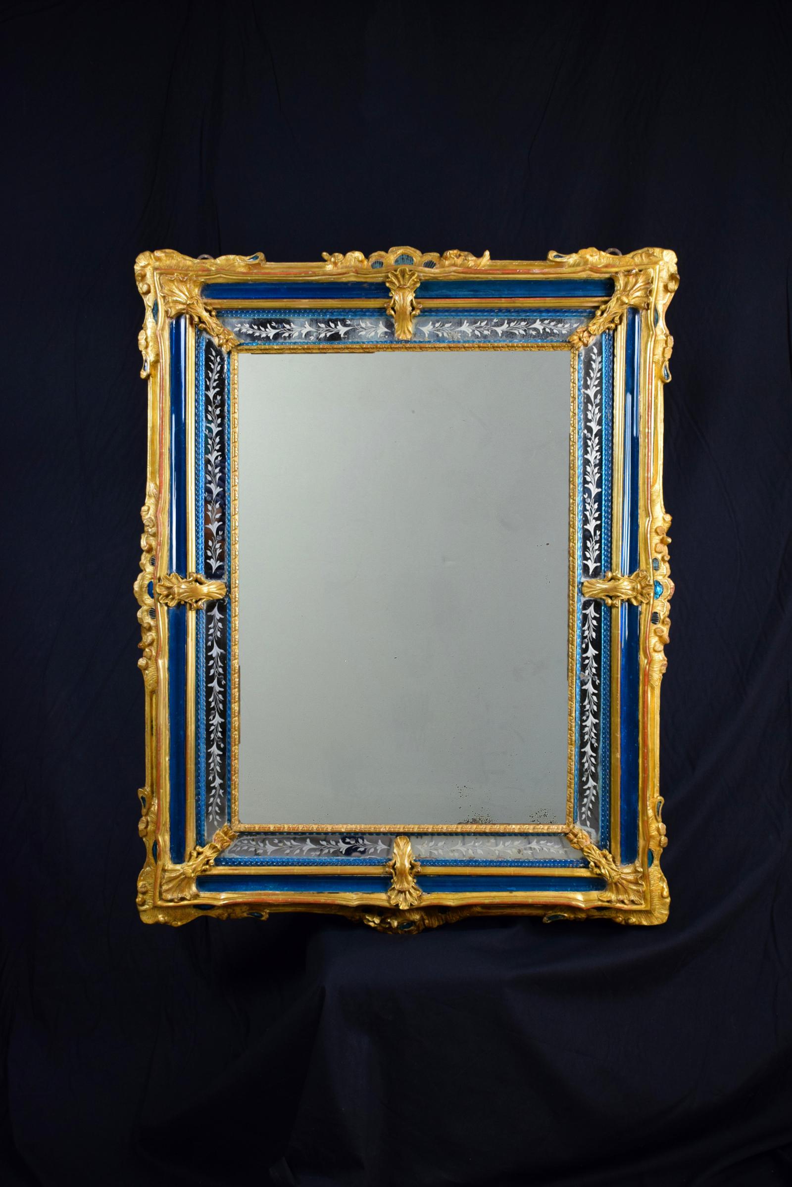 The rare and exquisite 18th century Venetian wall mirror is done of rectangular finely carved and gilded wood. It presents, on the corners, decorations with foliate motif. In the inner borders are included some original blue Murano’s glass paste