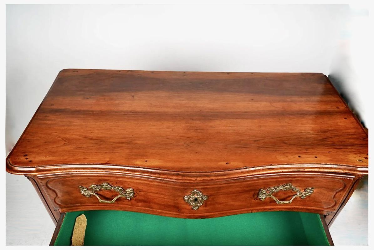 This is a very good provincial period Regence carved walnut commode or chest of drawers. The commode features an oxbow form with shaped drawers and a central drop pendant. The feet have stirrups and are in remarkably good original condition. The