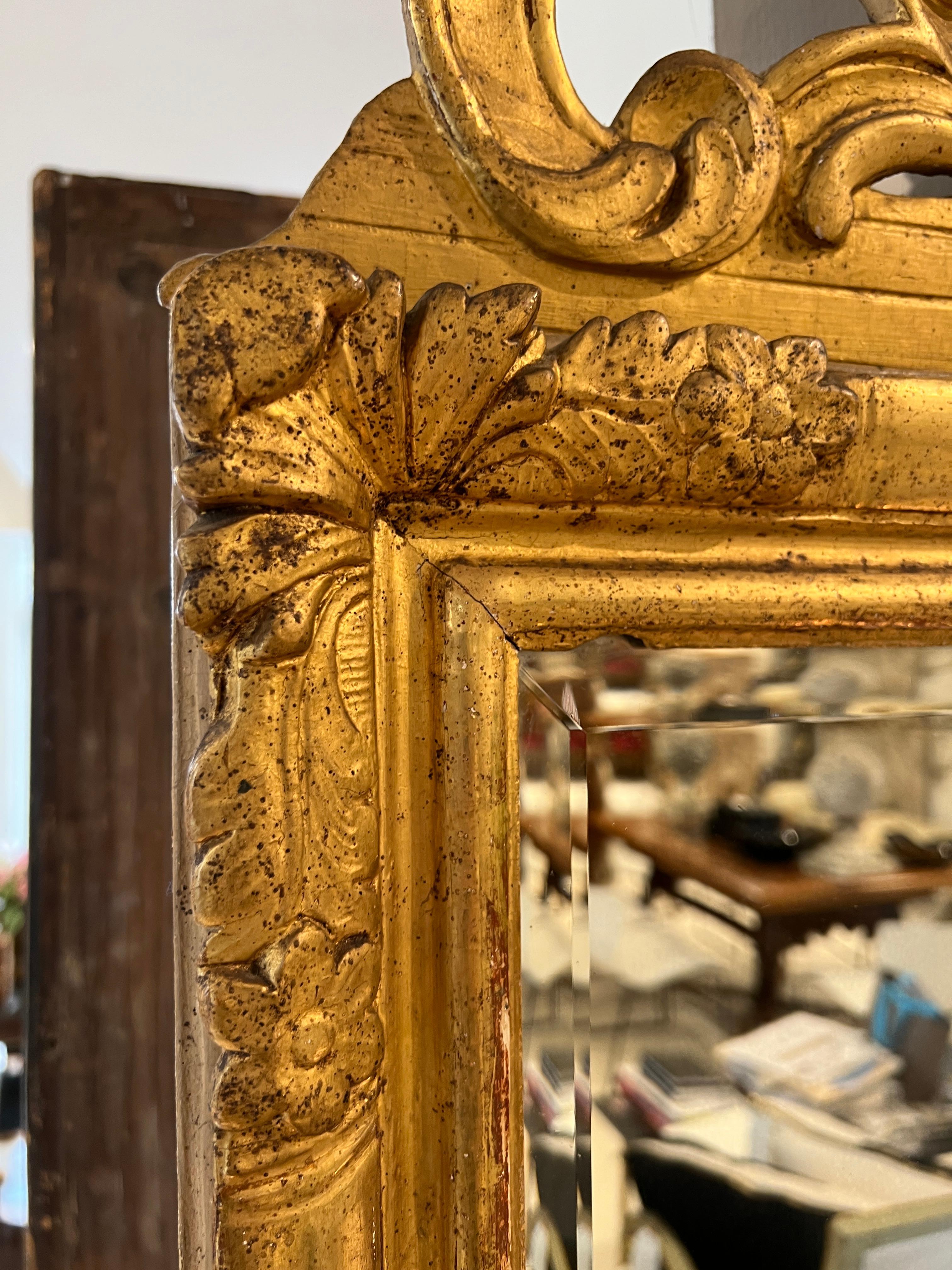 Ein verzierter Aufsatz aus vergoldetem Holz krönt einen rechteckigen Spiegel.  Viel vertikale Dramatik mit einem abgeschrägten Spiegel.