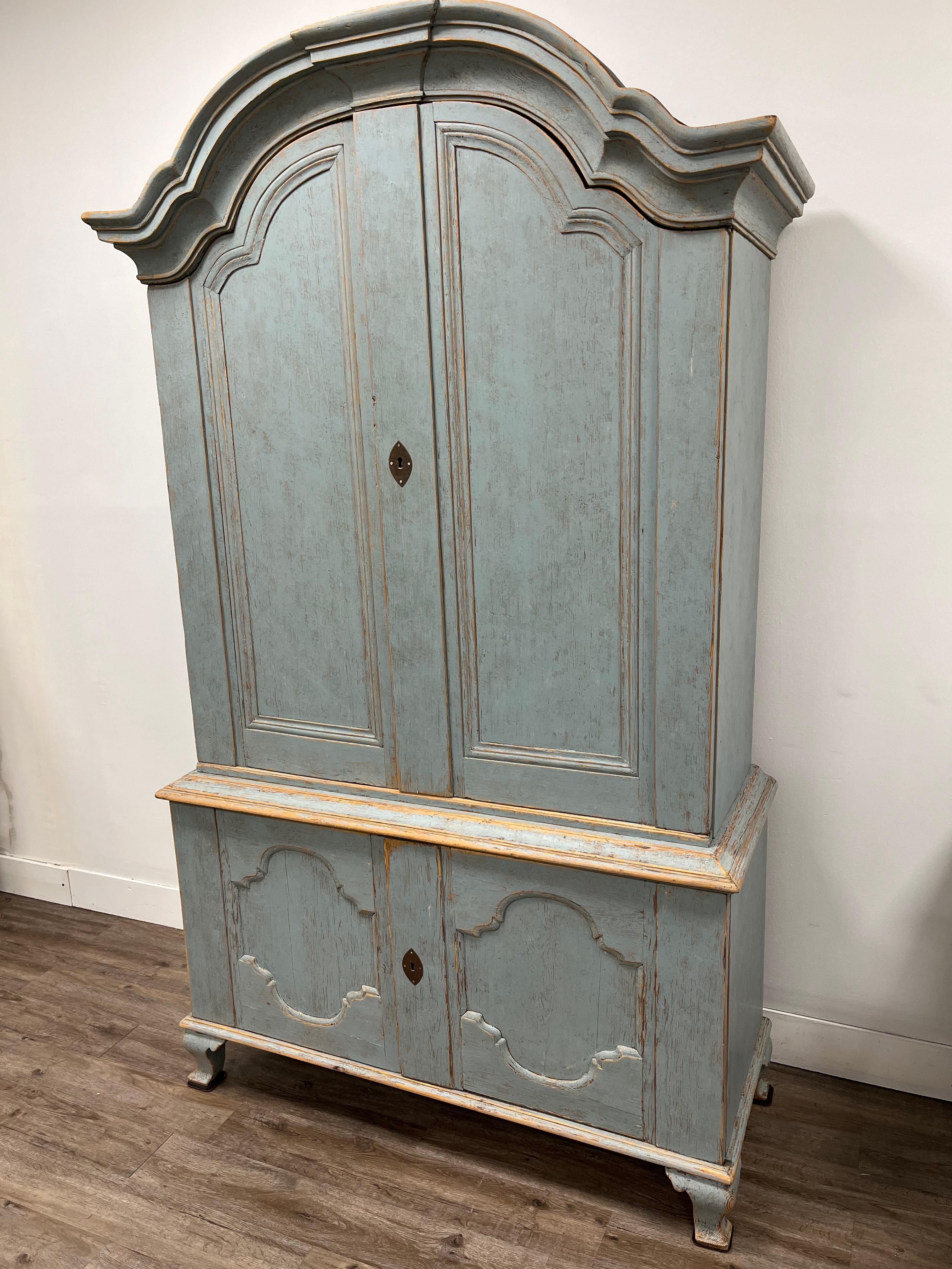 A Swedish Rococo cabinet from Varmland. The bonnet top consists of an impressive overhanging arched pediment cornice. Upper section has four shelves and five small drawers (with simple pulls) located between the second and third shelves. Lower