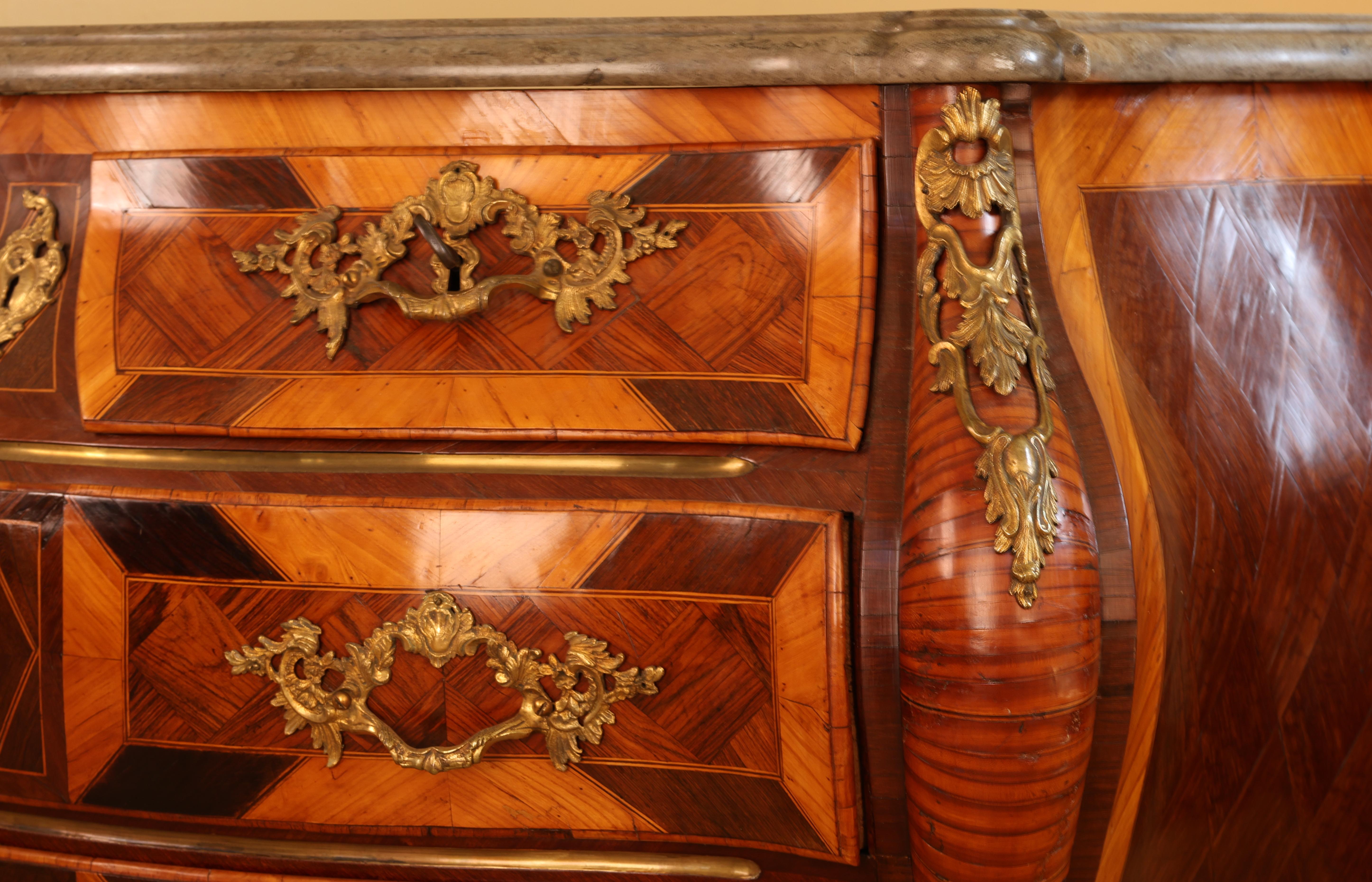 Un pezzo rococò di Stoccolma, realizzato da Ludwig Neijber il Vecchio. Il mobile è impiallacciato in legno di amaranto, jacaranda e prugna. Gli accessori e le decorazioni rocaille sono dorati a fuoco. La parte superiore è realizzata in pietra