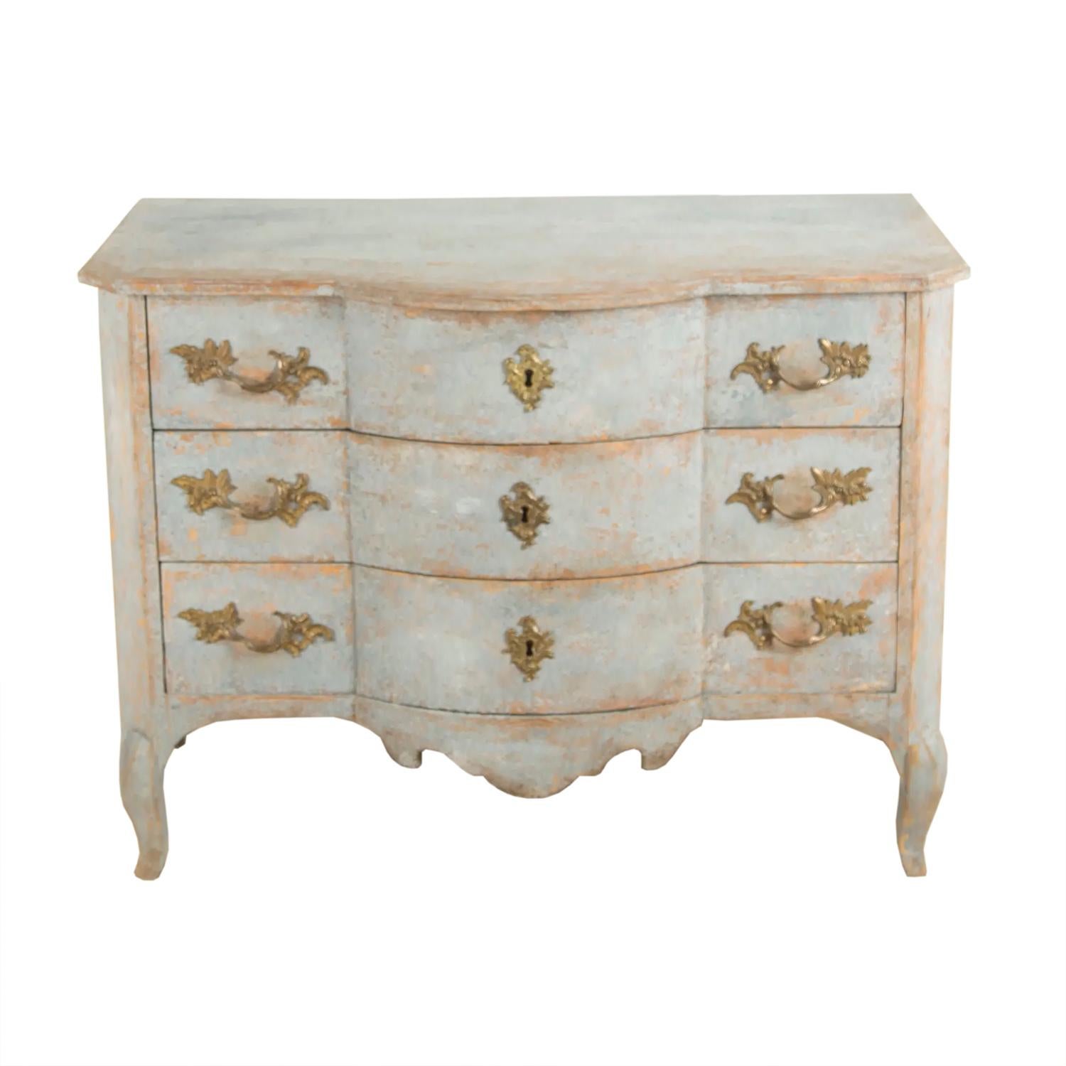 This 18th century Rococo commode features a bow front to the top and three long storage drawers, each with two ornate handles and keyhole. The commode tapers to cabriolet legs. This piece has been repainted, with original hardware.
