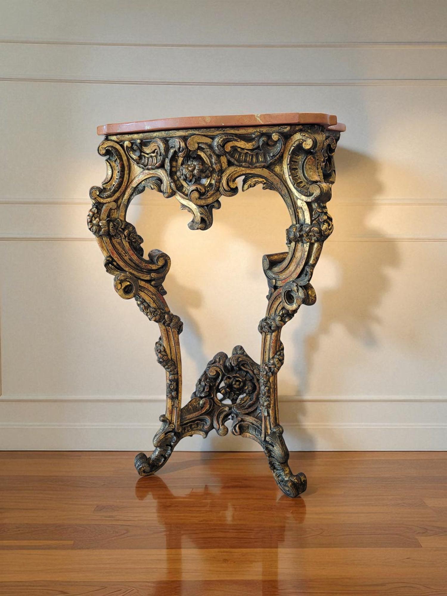 Cette console murale en bois doré de la fin du XVIIIe siècle présente des sculptures asymétriques élaborées avec des lignes fluides, des volutes et des motifs naturalistes tels que des fleurs et des feuilles, reflétant le mouvement et les éléments
