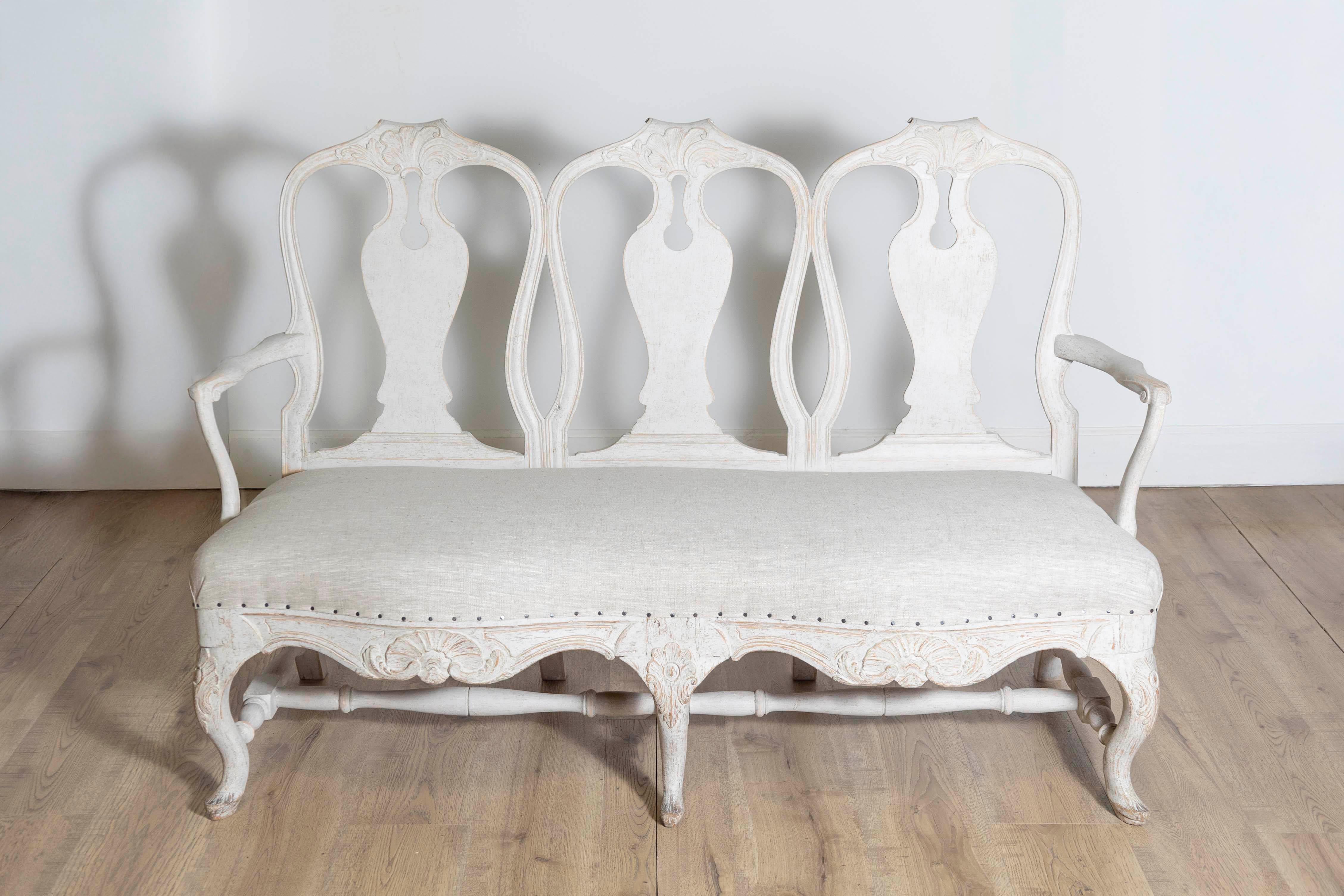 Ce canapé rococo suédois du XVIIIe siècle, vers 1760, incarne l'élégance et l'art de la période rococo. Fabriqué en bois sculpté à la main, probablement du hêtre ou du pin, il présente une finition peinte qui met en valeur les courbes délicates et