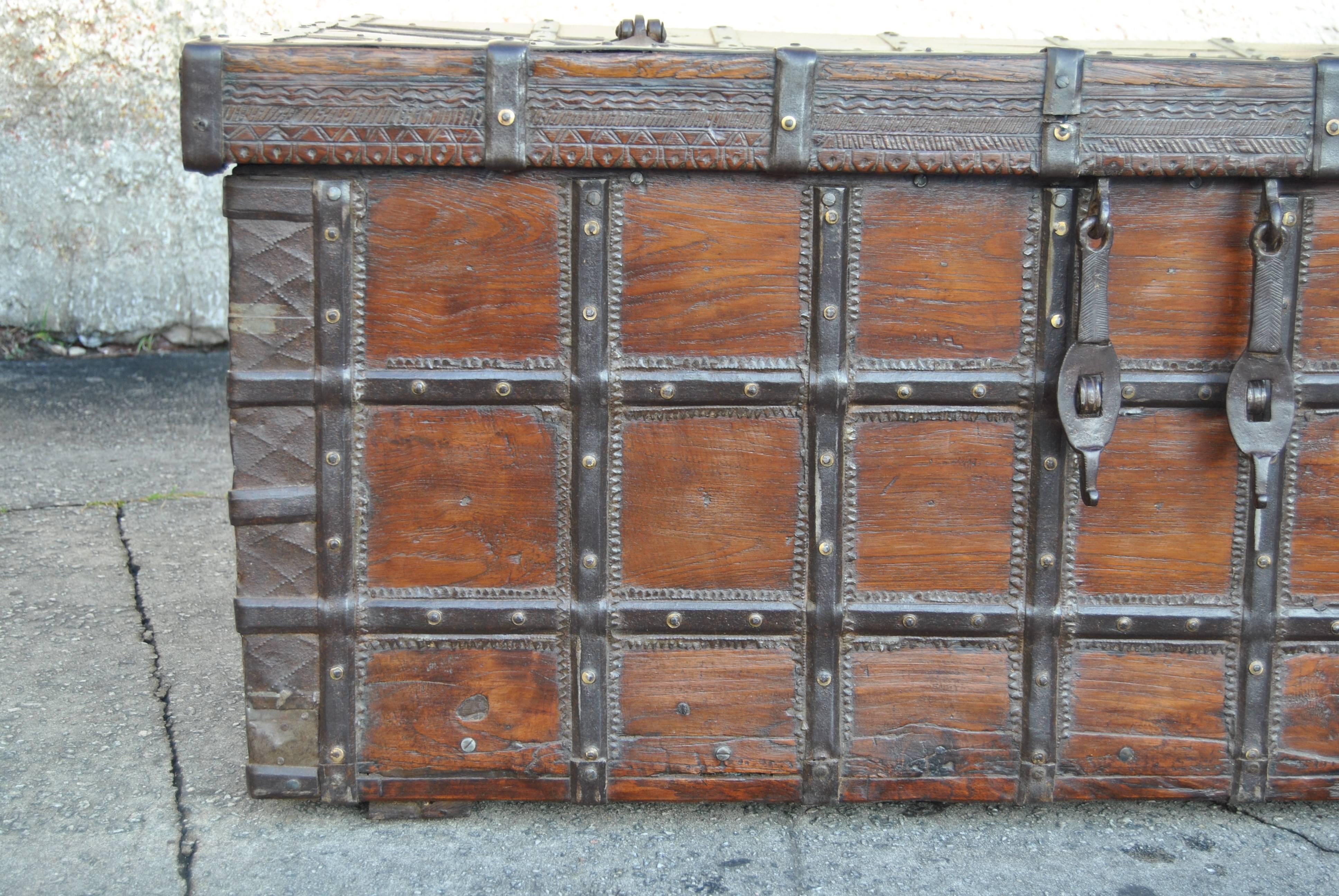 This is a blanket chest from India, made circa 1780. All the metal strapping, handles and lock clasps are handmade of hand-forged iron. There is beautiful hand carving around the bottom edge of the top of the chest. On the right and left front sides