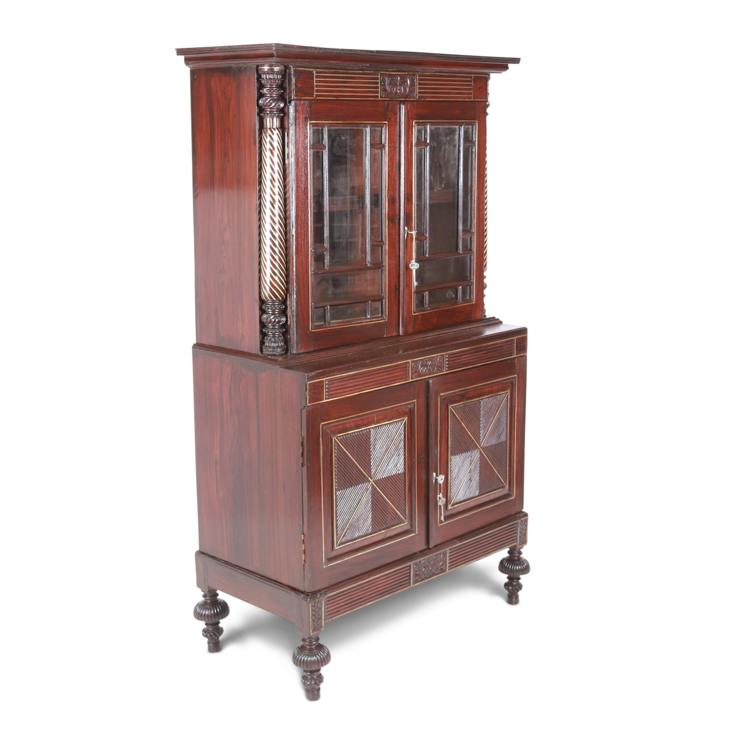 An 18th-century Rosewood Dutch Colonial cabinet of exceptional quality, with brass inlays gracing the top section, side columns, door panels, and turned feet base. It has beautiful reeded carved details on the doors and is very well made. 