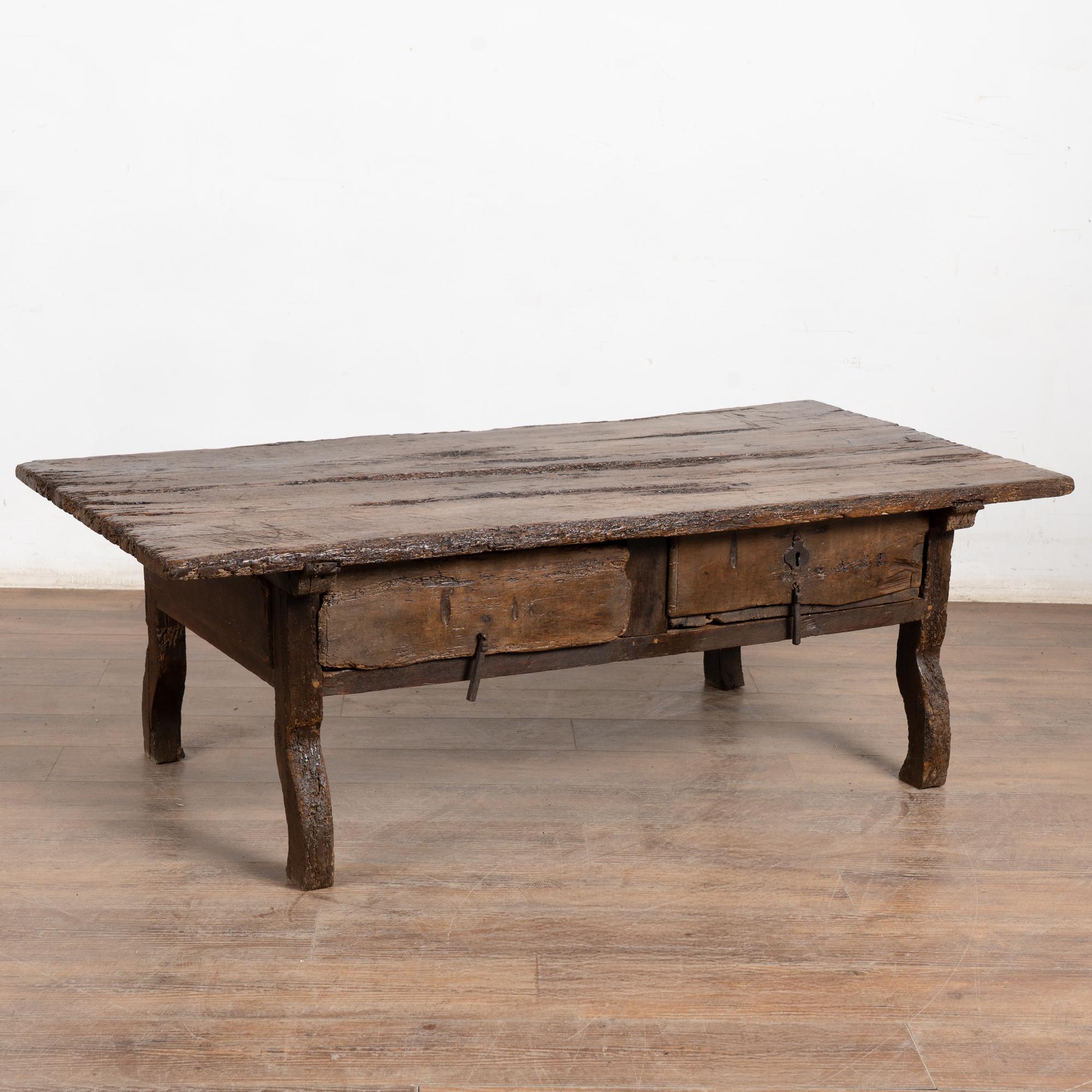 Cette table basse rustique en chêne foncé comporte deux tiroirs avec des poignées en fer. L'usure et la détérioration importantes confèrent à cette table son caractère remarquable. Le plateau, les tiroirs et les pieds en forme d'arc-en-ciel