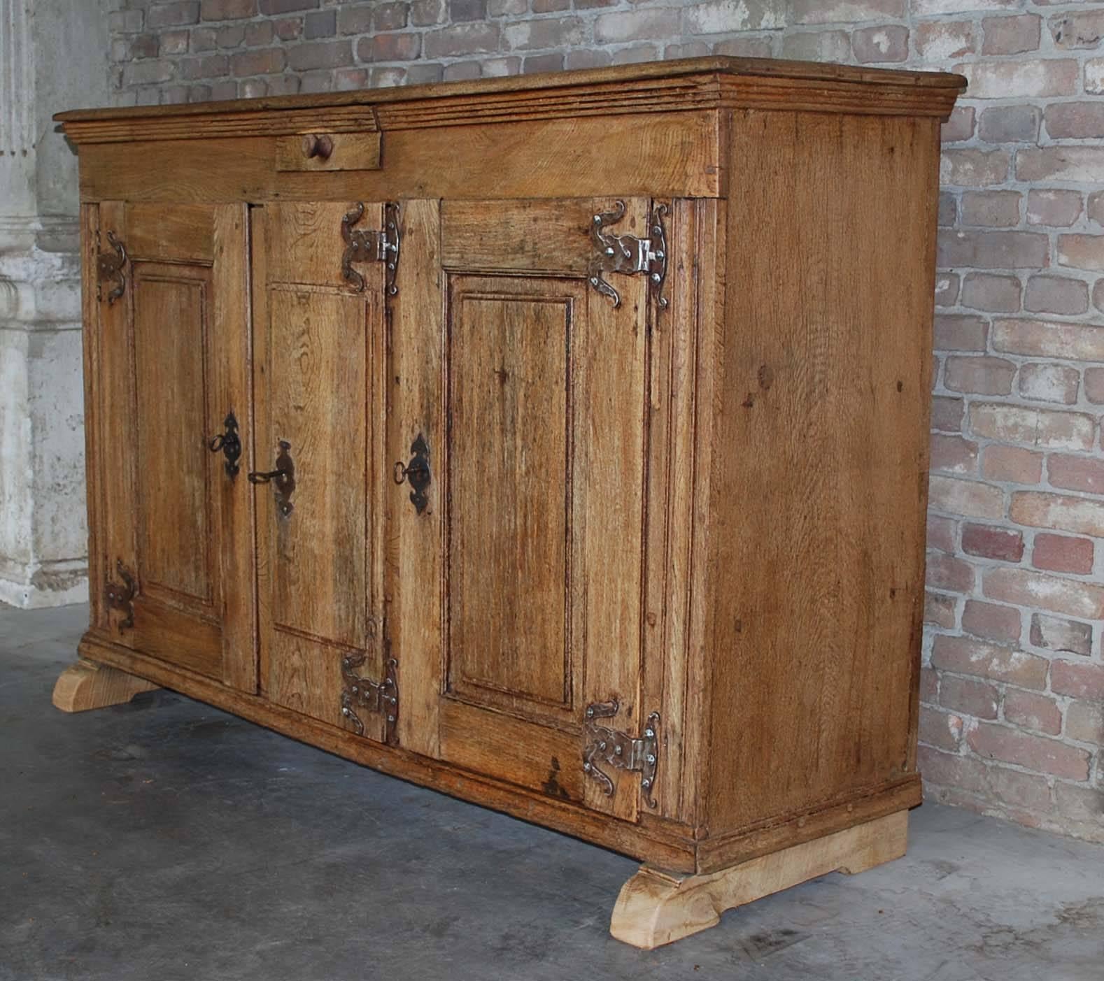 An attractive buffet base with three doors and one drawer. It has two doors with raised panels and one more narrow solid door.
All three doors can be locked, three keys included. It has hand-forged snake hinges. Per compartment there are two fixed