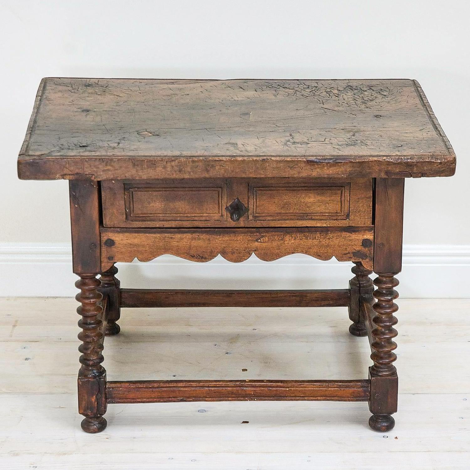 Dieser kleine, rustikale spanische Schuhmachertisch (mesa de zapatero) aus dem 18. Jahrhundert wurde, wie viele dieser traditionellen Möbel, aus massivem Nussbaumholz handgefertigt. Die Tischplatte besteht aus einem einzigen Brett und weist