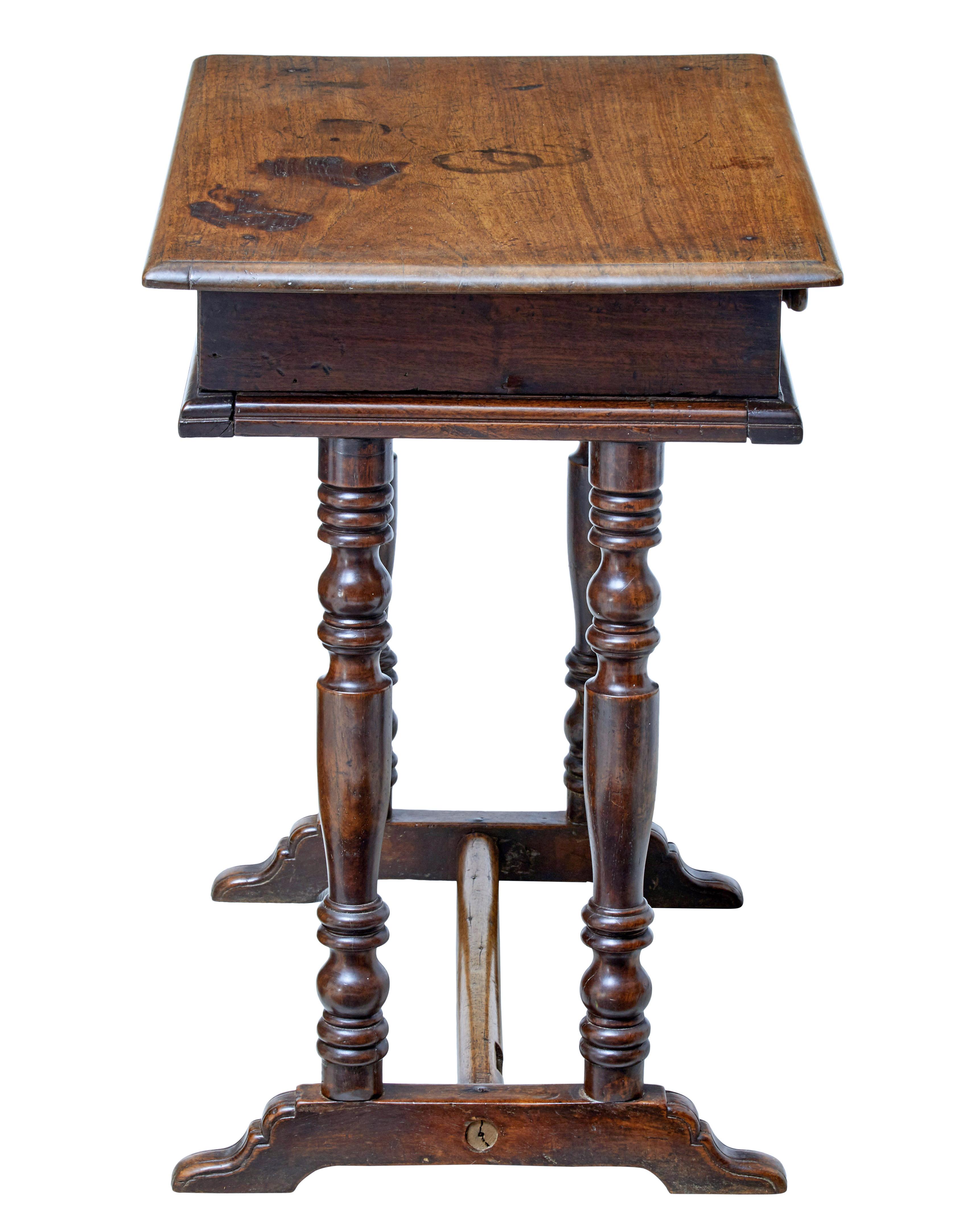 Quirky rustic walnut side table, circa 1780.

Over-sailing top beneath which is a single drawer with 2 turned handles.

Standing on 4 turned legs and sledge feet, united by stretcher.

Lock missing to drawer, surface burns and staining to top,