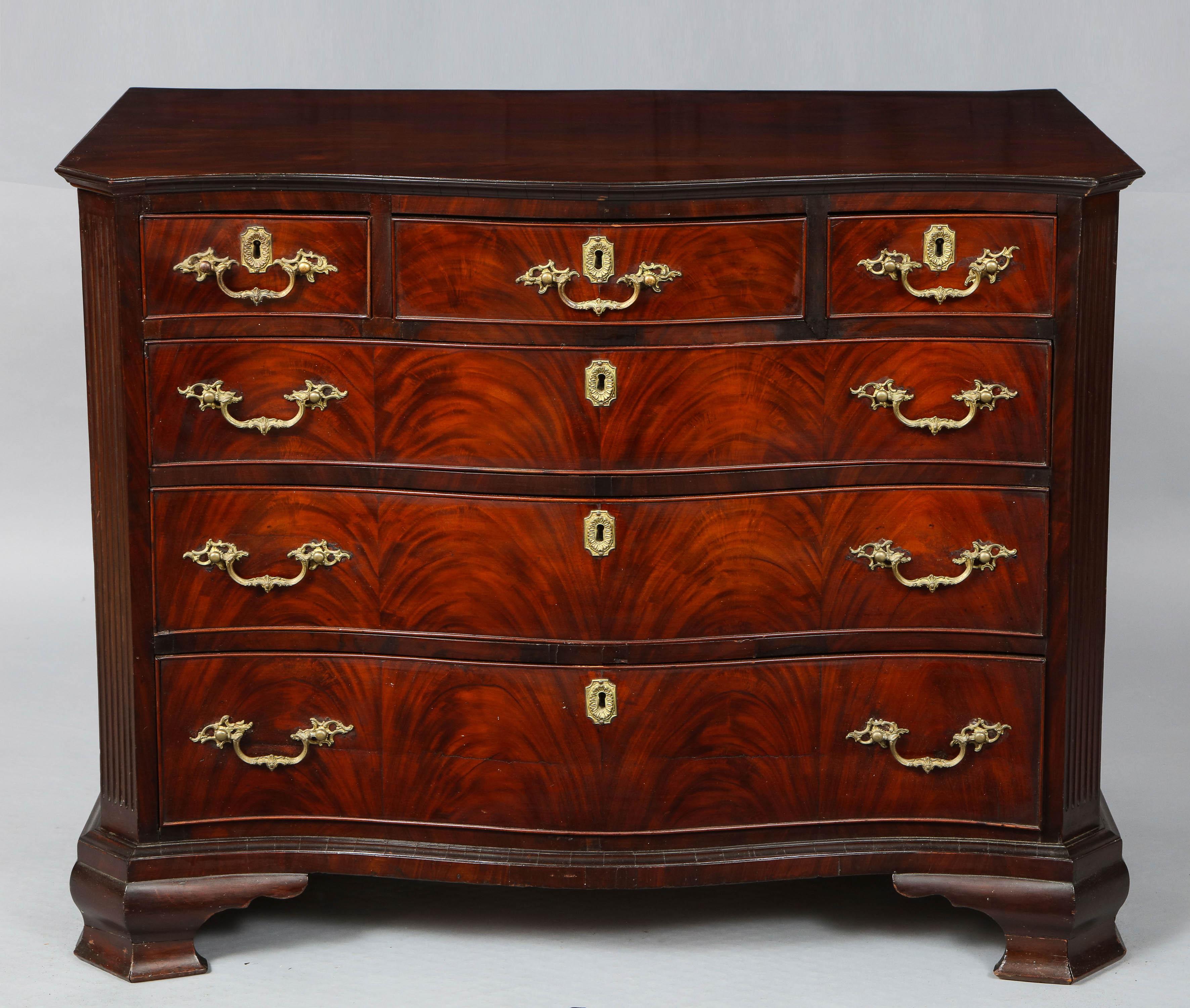 Fine 18th century English mahogany serpentine fronted chest with fluted canted corners, the well figured top with segmented under edge molding over three short drawers, the center one fitted with pullout / pull-out writing surface and side drawer,