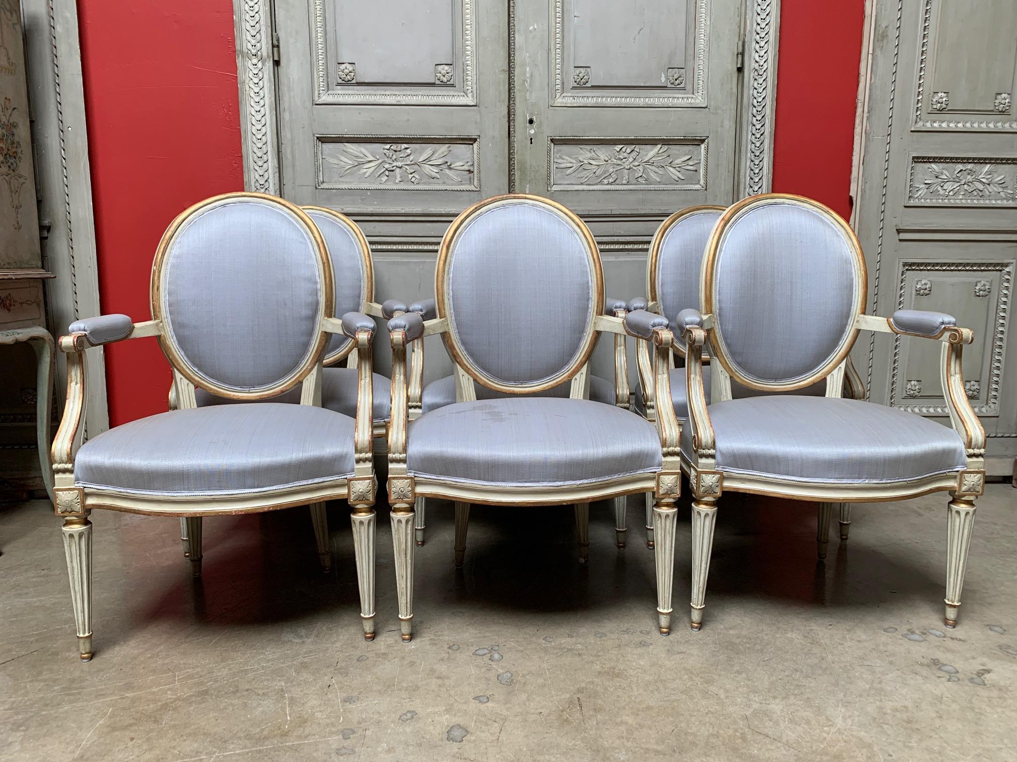 Six French Louis XVI pale gray painted and parcel-gilt dining armchairs from the late 18th century. These fauteuils are beautifully carved with oval backs and flutted legs. The painted and gilt fininsh is recently done, but the frames are of the