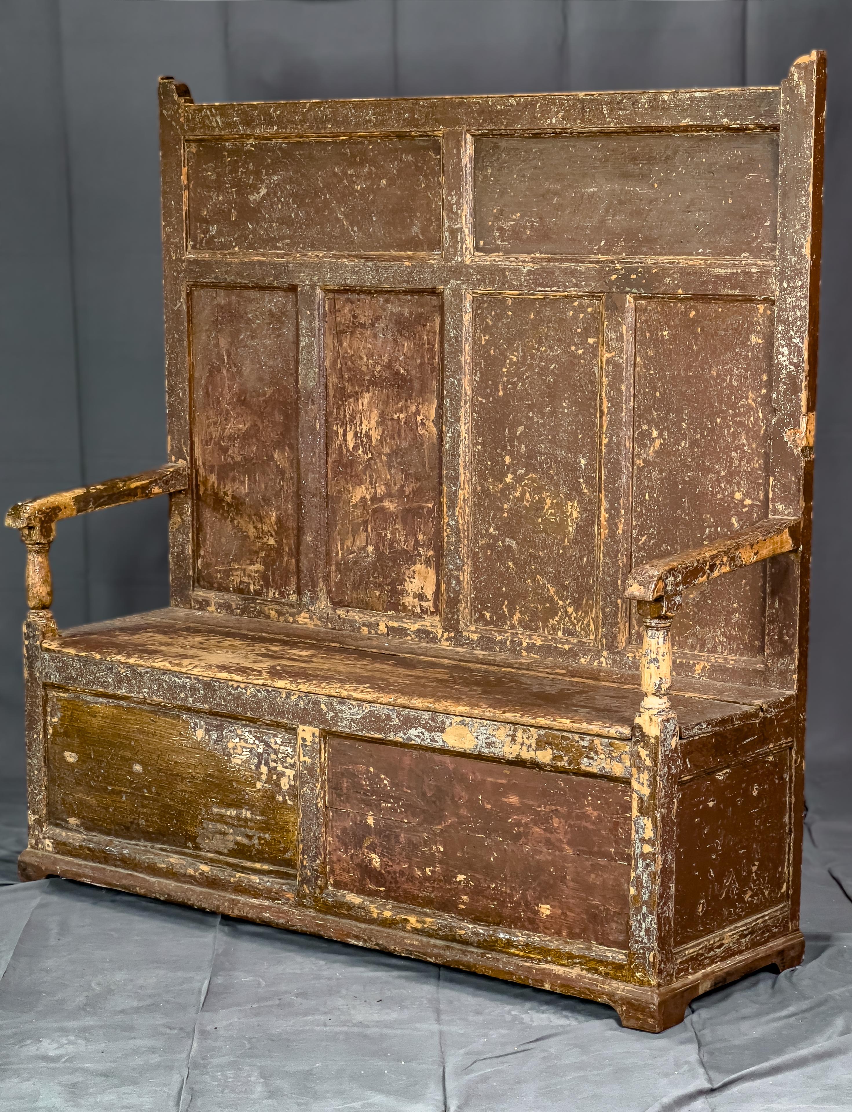 18th Century Settle bench. Originally the finish was stained like most items, and either the bench was exposed to the elements against a wall or the bench was modified to have the distressed look. In the front Paneled detail and a lift seat for