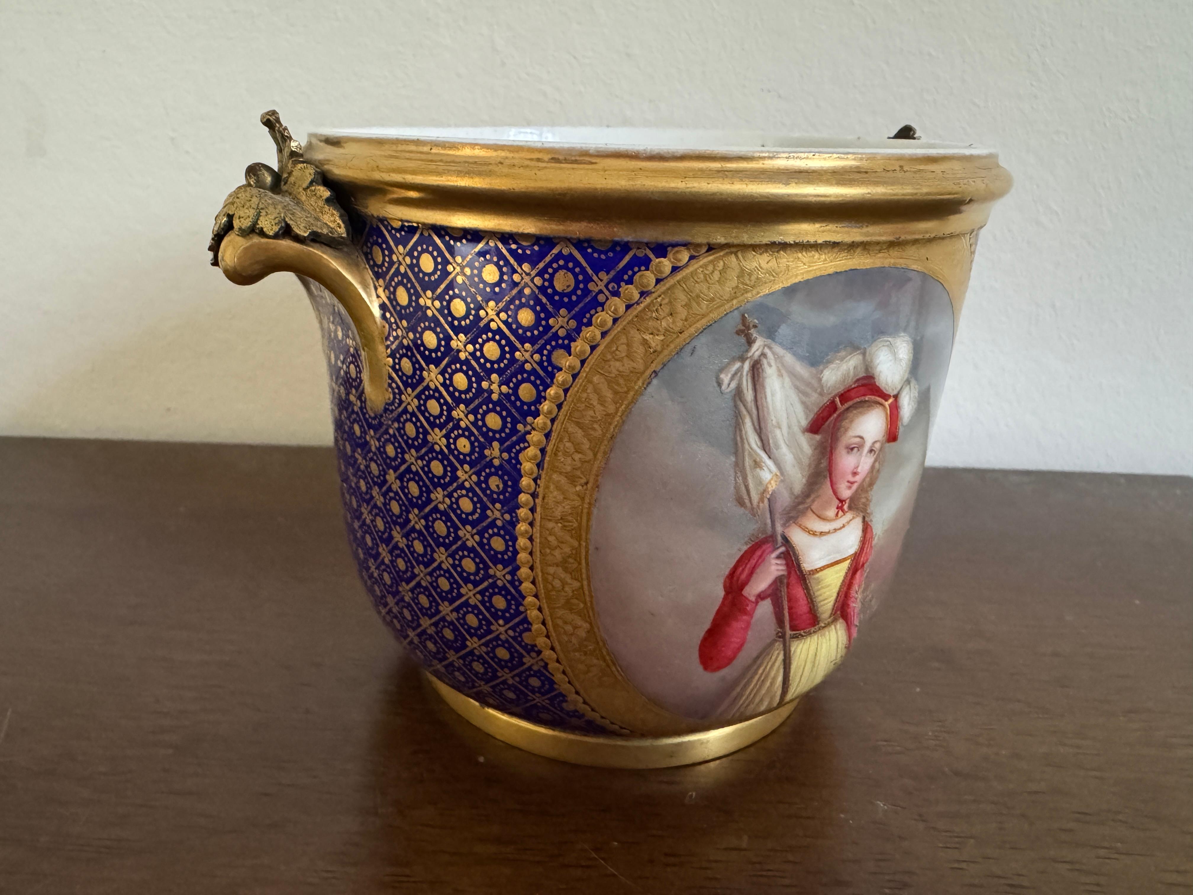 Seaux à bouteille du 18e siècle, de style Sèvres, sur fond bleu et monté en métal doré. Le corps sur fond bleu est orné de deux panneaux ovales peints opposés dans un cadre en treillis doré et à motifs de points, un panneau peint en couleurs