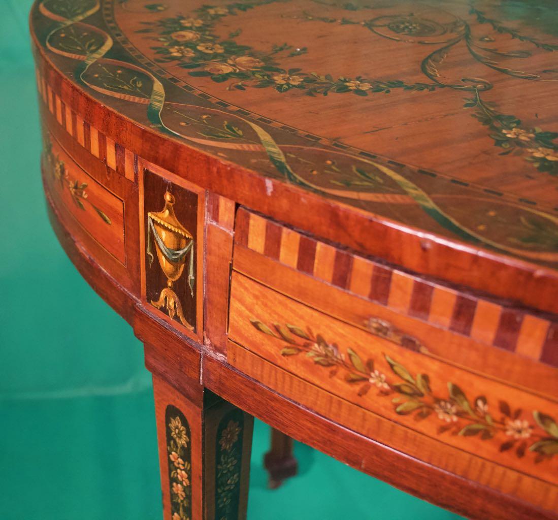 A fantastic Sheraton George III oval writing tables, elegant appearance, in satinwood and painted with floral garlands and with central panel with figures of Venus and Cupid, period 18 century.

The neoclassicism of Sheraton is characterized by the