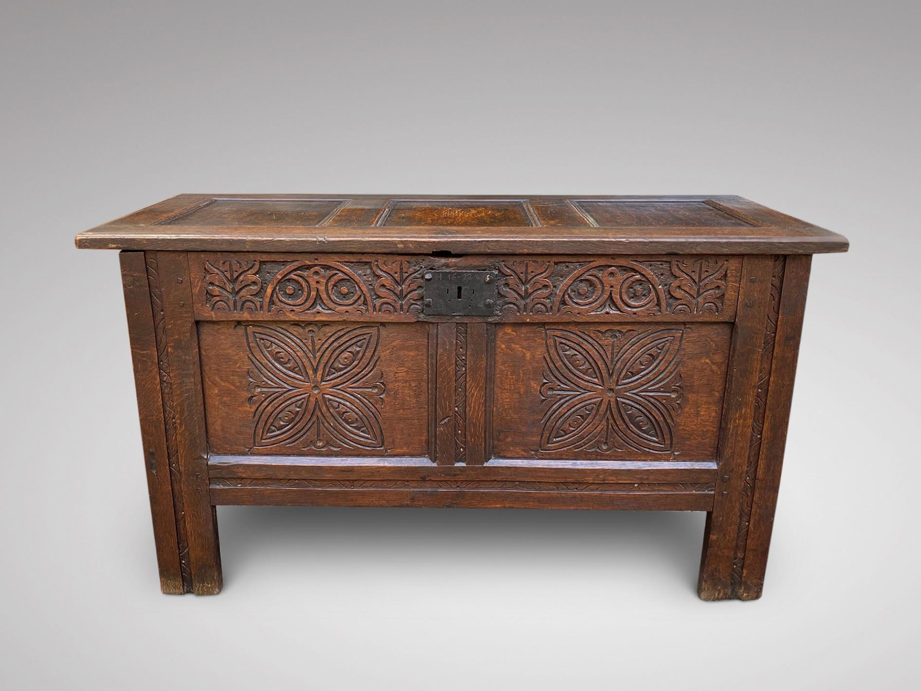 A small early 18th Century oak antique coffer, trunk, chest. The single plank rectangular top with above a carved frieze with two lozenge carved panels with further carved detail to the stiles, having planked ends and of lovely colour and
