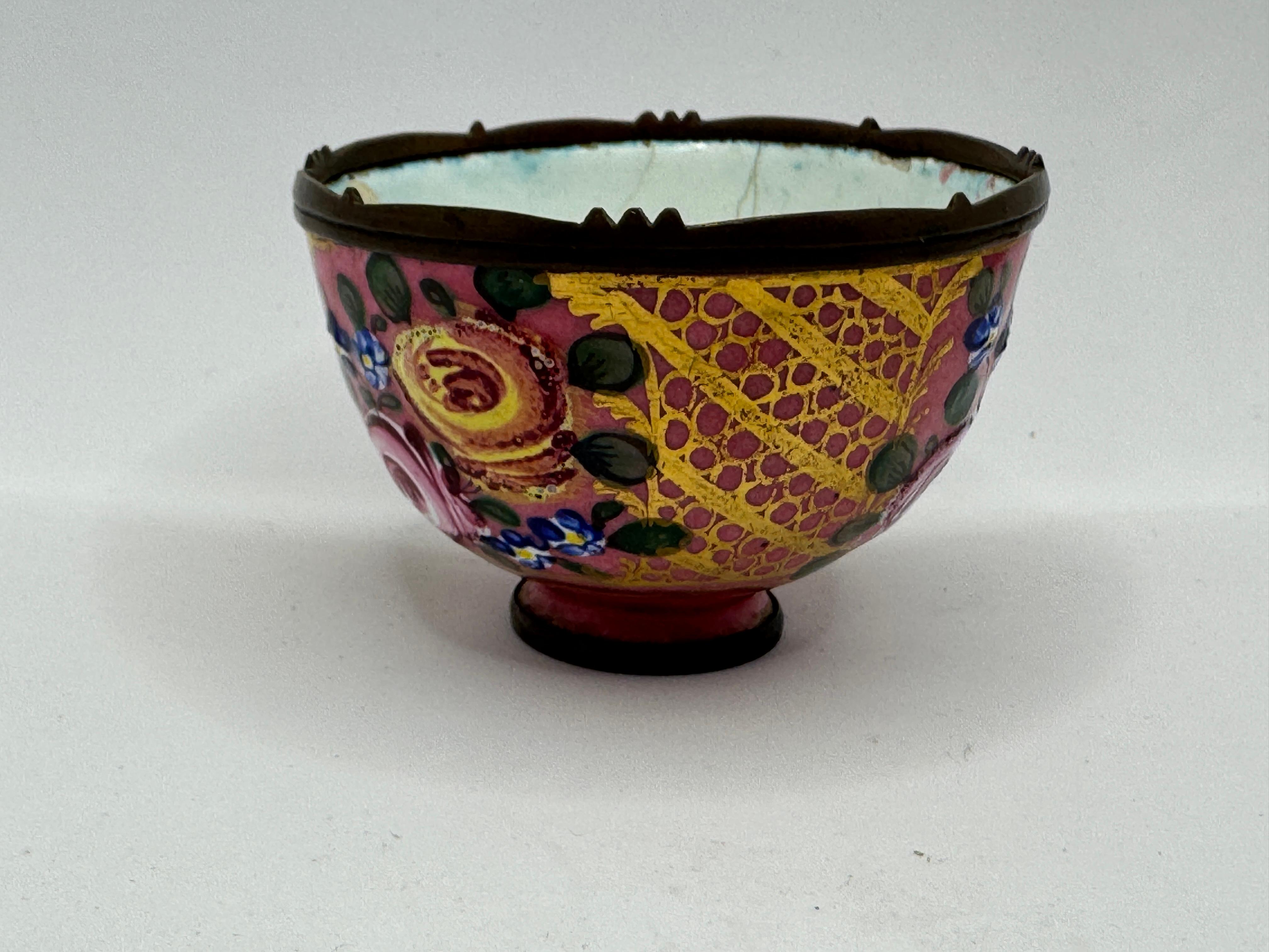 Salero pequeño de Limoges esmaltado de finales del siglo XVIII, decorado con un fondo rosa enrejado amarillo y motivos florales pintados a mano (rosas, flores azules, hojas verdes), un reborde metálico con dientes intermitentes en la parte superior