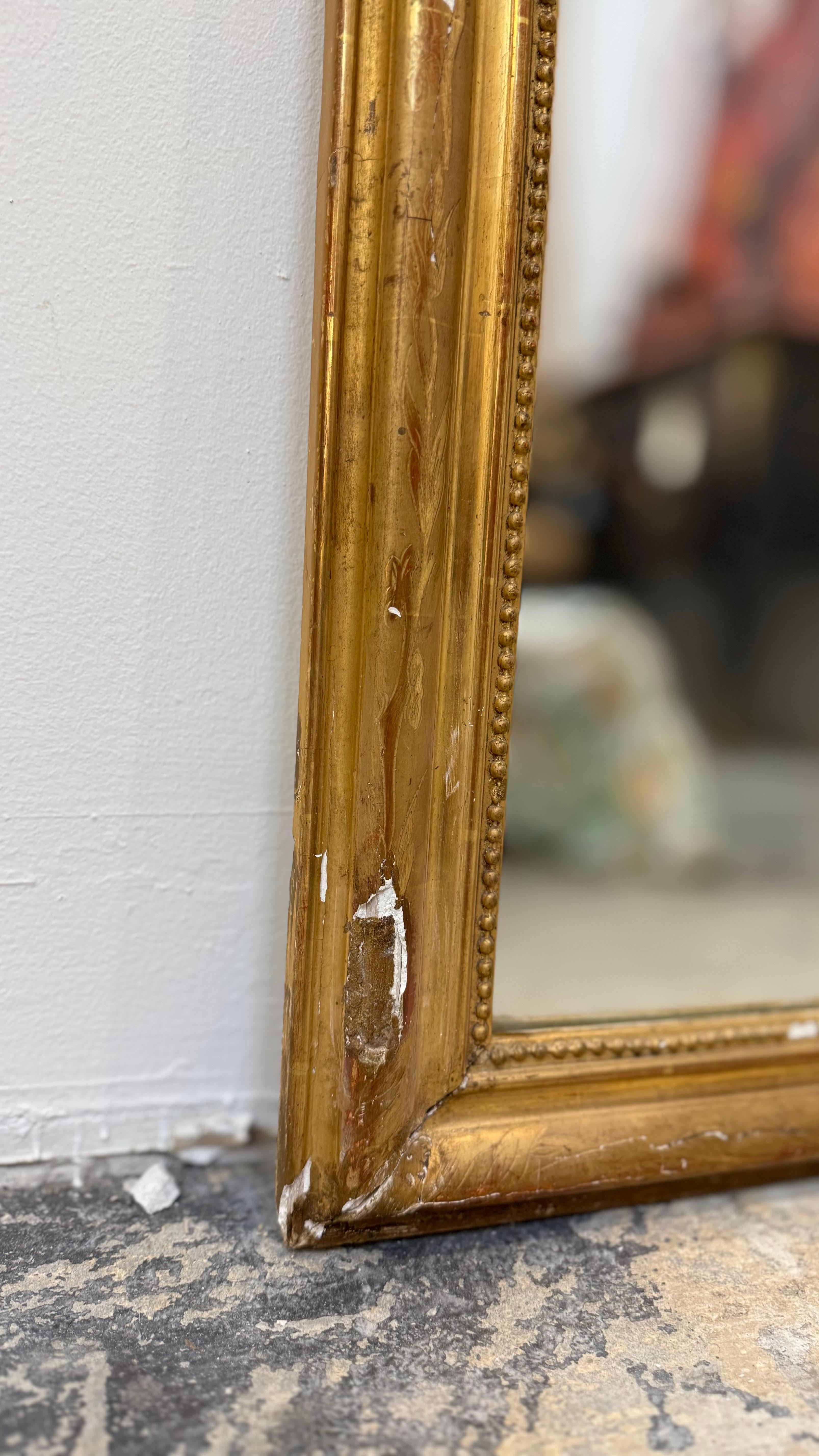 Ce charmant miroir de style Louis XVI du XVIIIe siècle est une relique raffinée du goût néoclassique français. Il est fabriqué en bois doré sculpté, avec des coins doux et arrondis et un sommet légèrement arqué. Le cadre présente de délicates perles