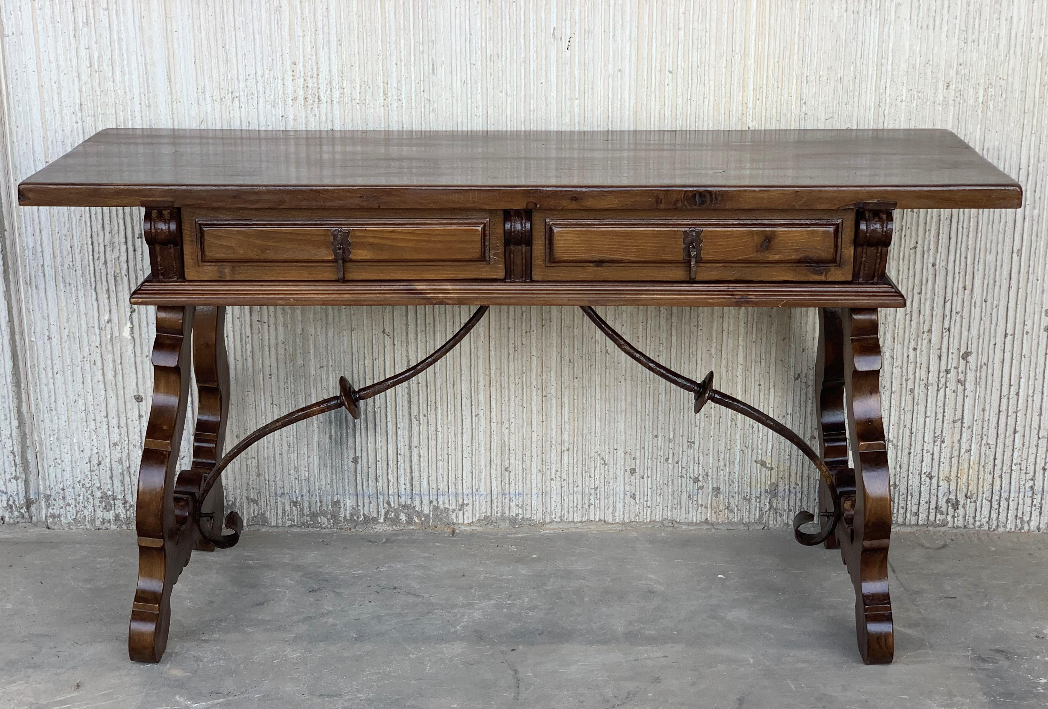 An 18th century Spanish baroque desk, or writing table made of solid walnut with lyre shaped legs joined by wrought iron stretchers. Hand carved decoration across the front and the back. Two drawers with original iron drawer pulls. The top is made