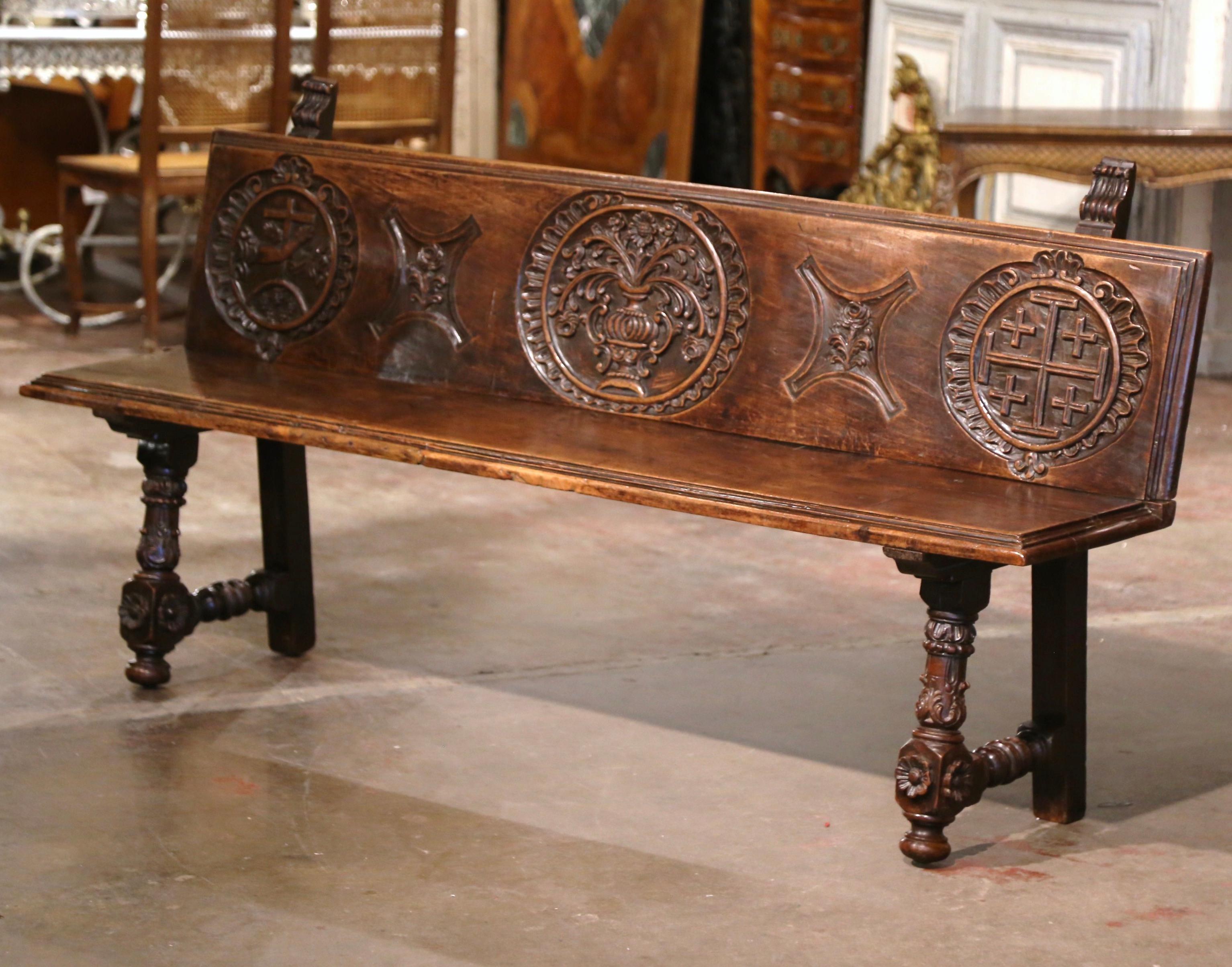 Add extra seating to a hallway, den or living room with this elegant antique bench with back and religious motifs. Crafted in northern Spain circa 1780, this sturdy fruit wood seating stands on carved turned legs decorated with acanthus leaves and