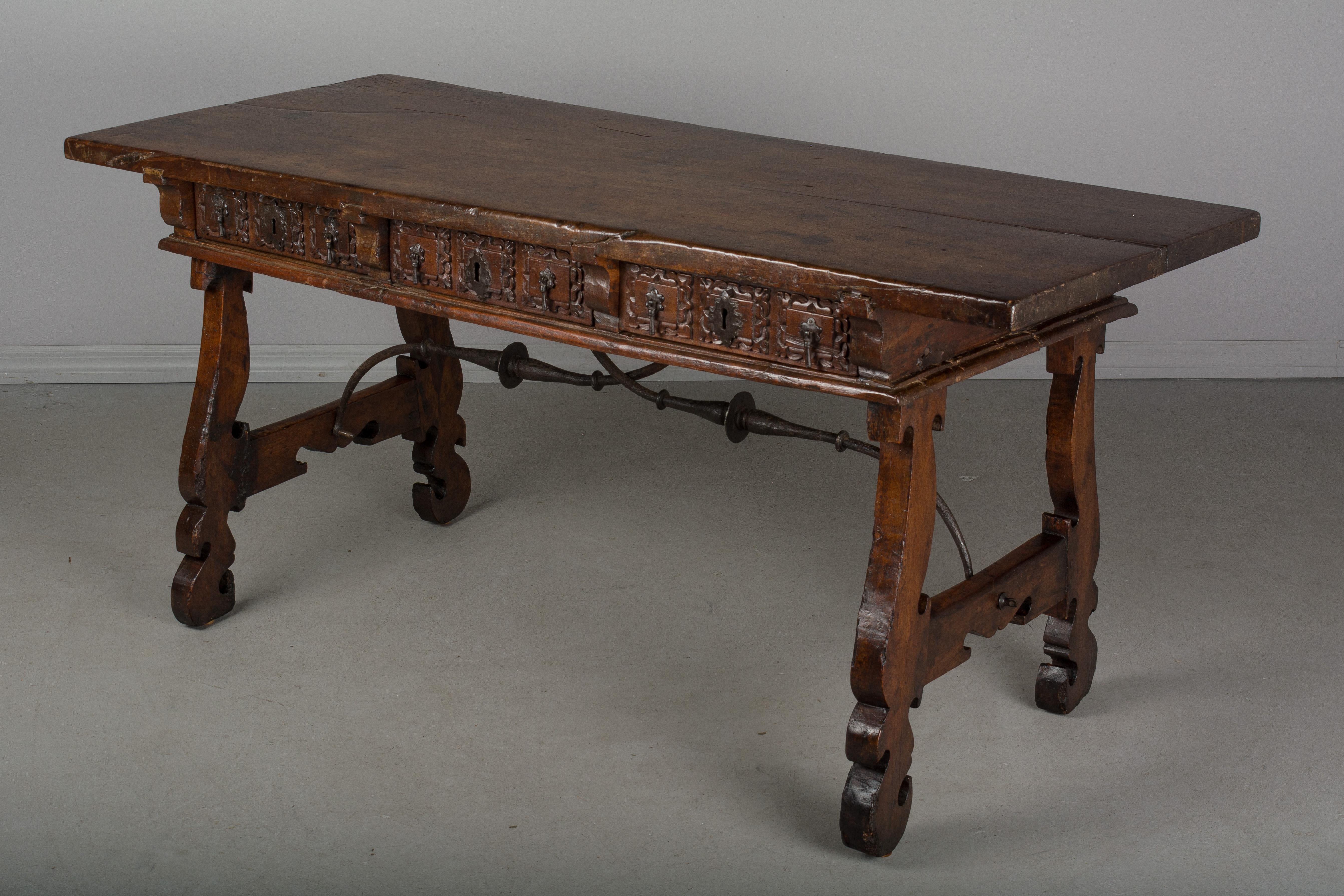 An 18th century Spanish Baroque desk, or writing table made of solid walnut with lyre shaped legs joined by wrought iron stretchers. Hand-carved decoration across the front and the back. Three dovetailed drawers with original iron drawer pulls and