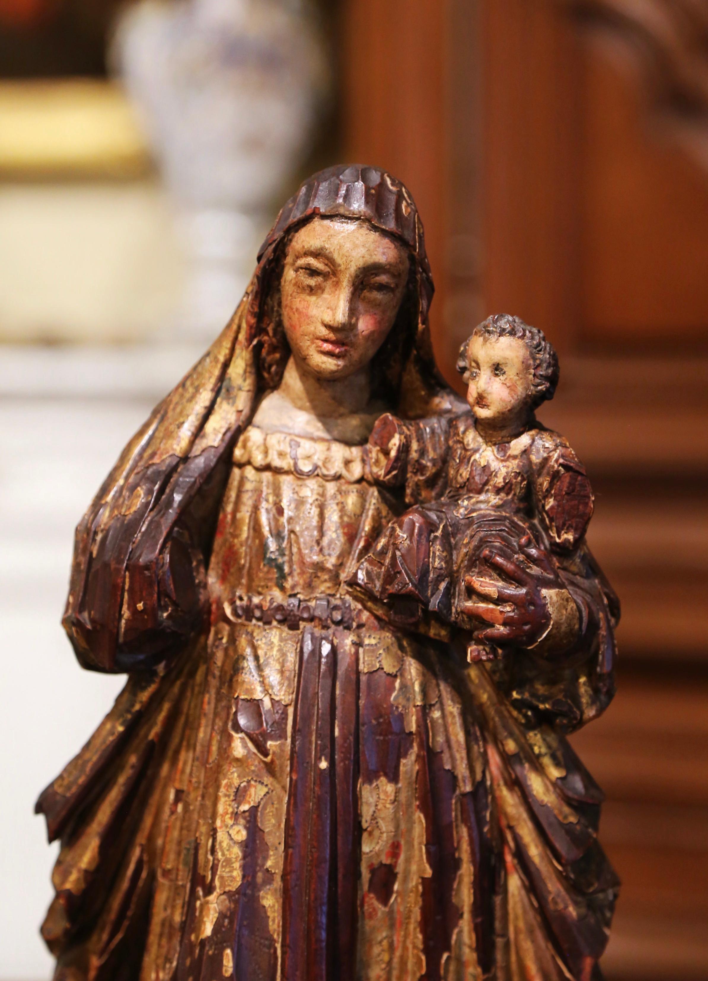 This antique religious figure was carved in Spain, circa 1760. The large alluring polychrome and gilt sculpture in high relief, depicts the Virgin Mary standing and carrying little Jesus in her left arm. The colonial santo figure has wonderful