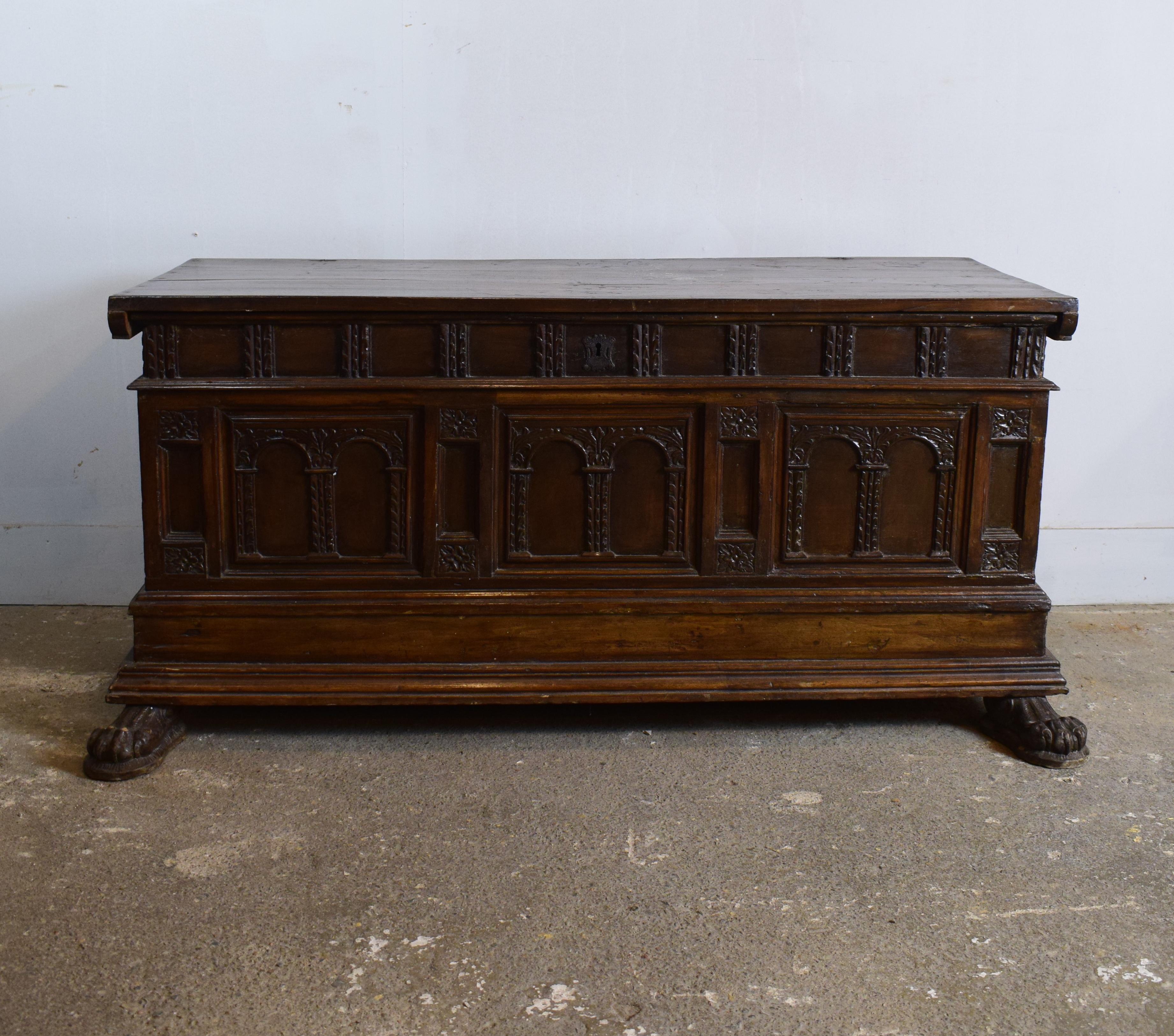 This Spanish features a long rectangular shape body which has a geometrical design carved into the side panels. In the front underneath the coffer are two carved paw feet that project out. The trunk interior offers a large open storage space which