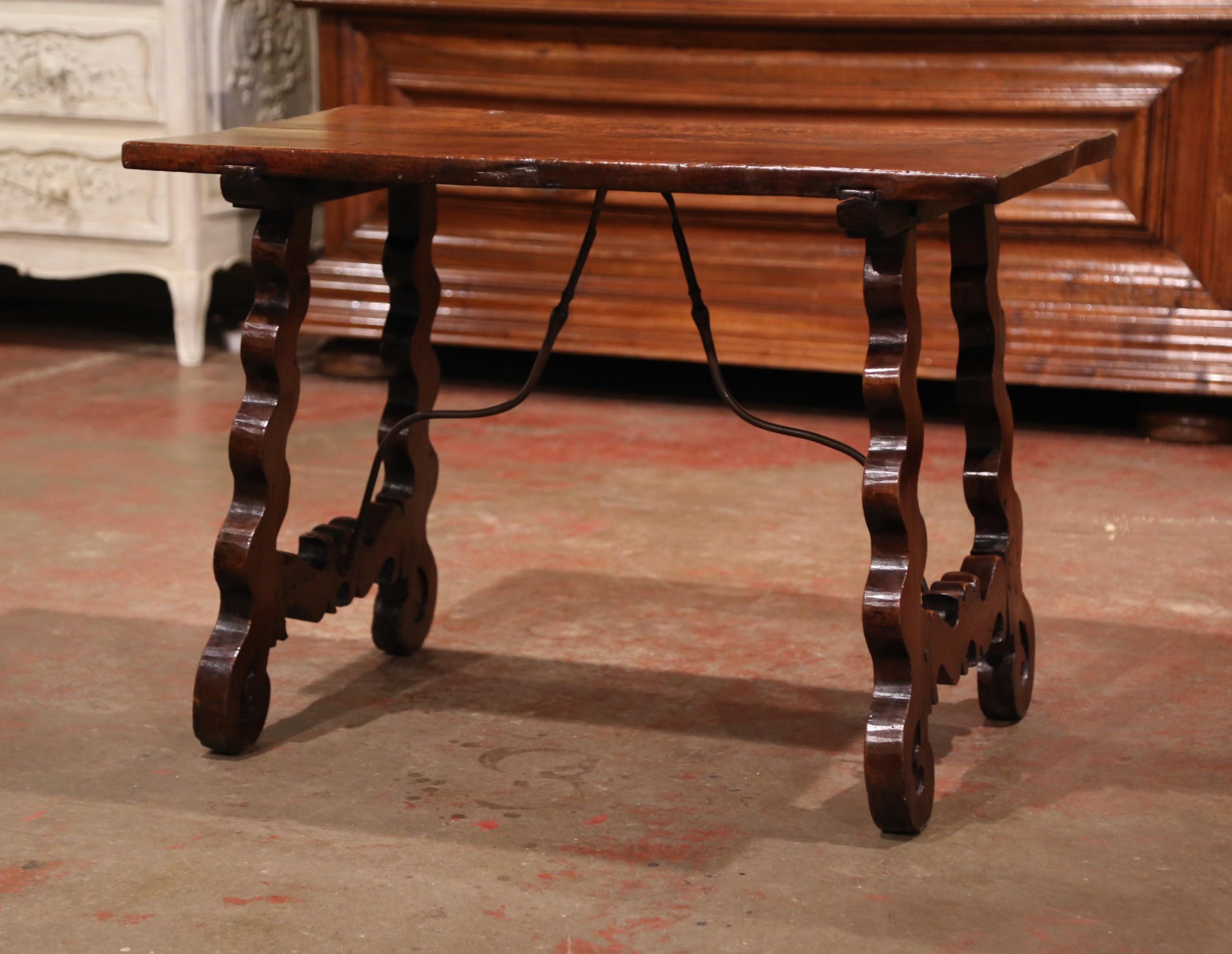This elegant antique table was crafted in Spain, circa 1780. Built in walnut, the small end table features two carved, A-shape legs, which are connected in the center with a forged black wrought iron stretcher for stability and structure; the