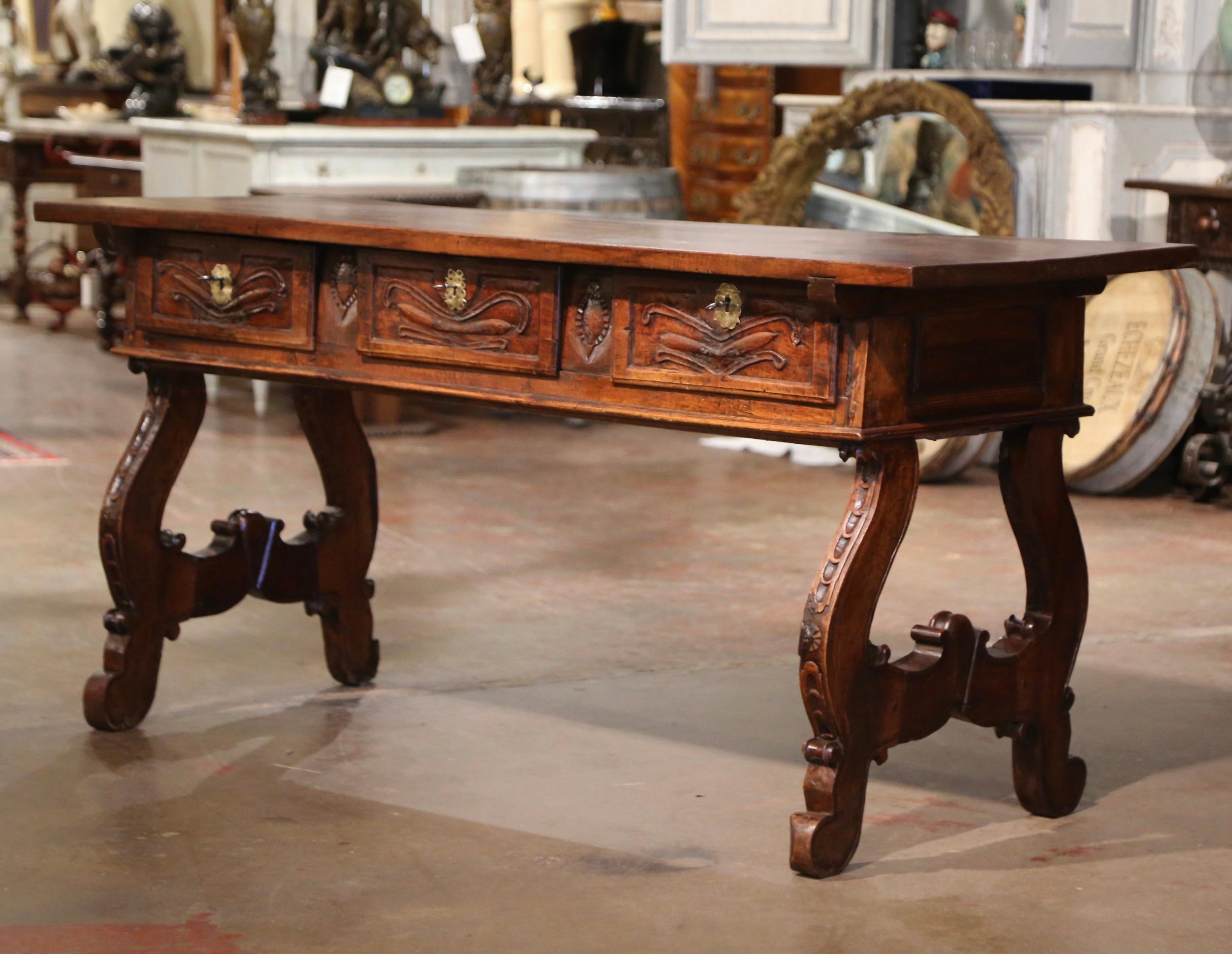 Add an elegant focal point to your study or library with this antique Spanish carved console. Carved in Spain circa 1750 and built of solid walnut wood, the trestle table stands on two intricate carved legs with scroll motifs. The desk is dressed