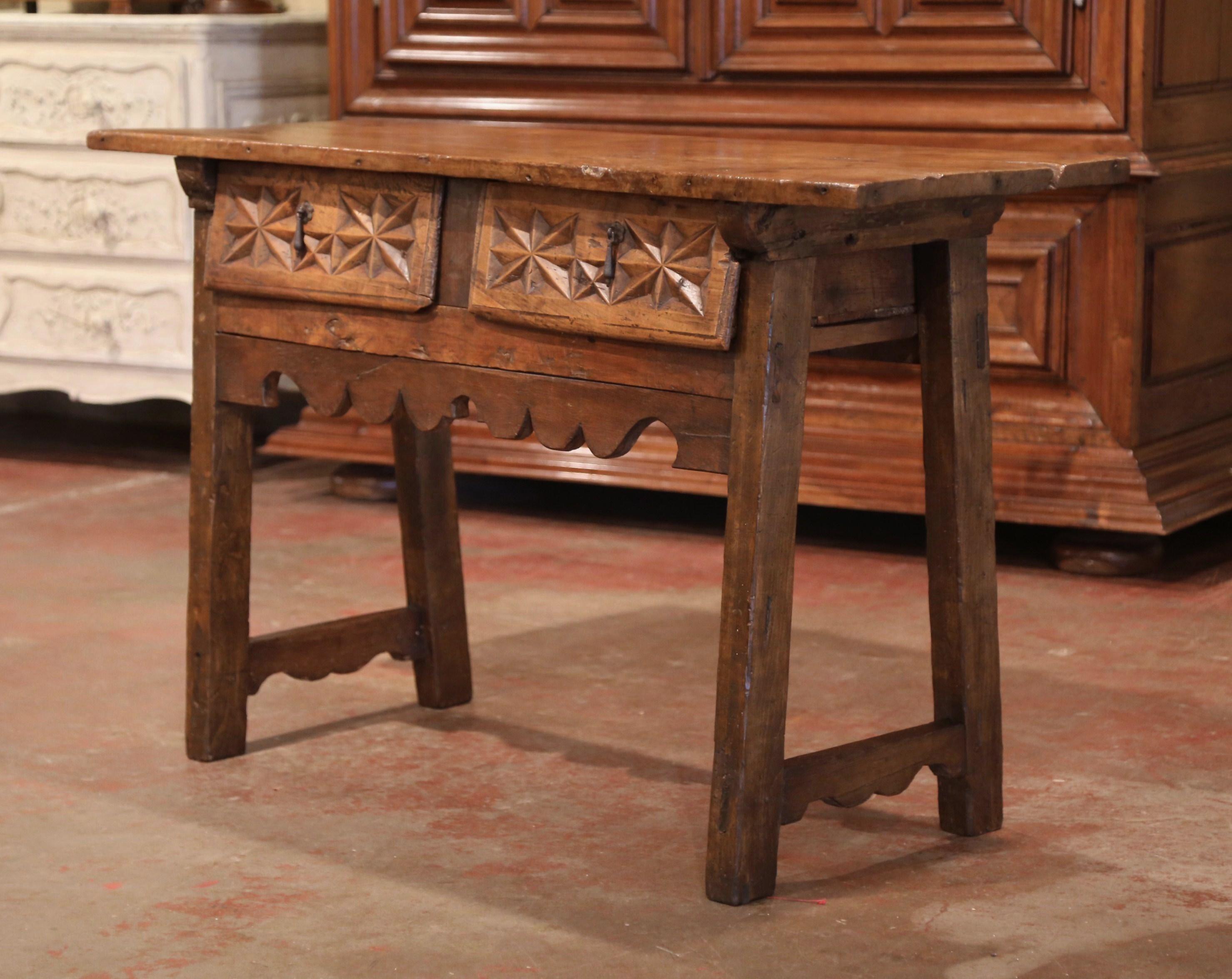 This elegant antique fruitwood console was crafted in Spain, circa 1750. The tall trestle table stands on four square slant legs over a scalloped front apron, the console features a pair of carved drawers across the front, decorated with geometric