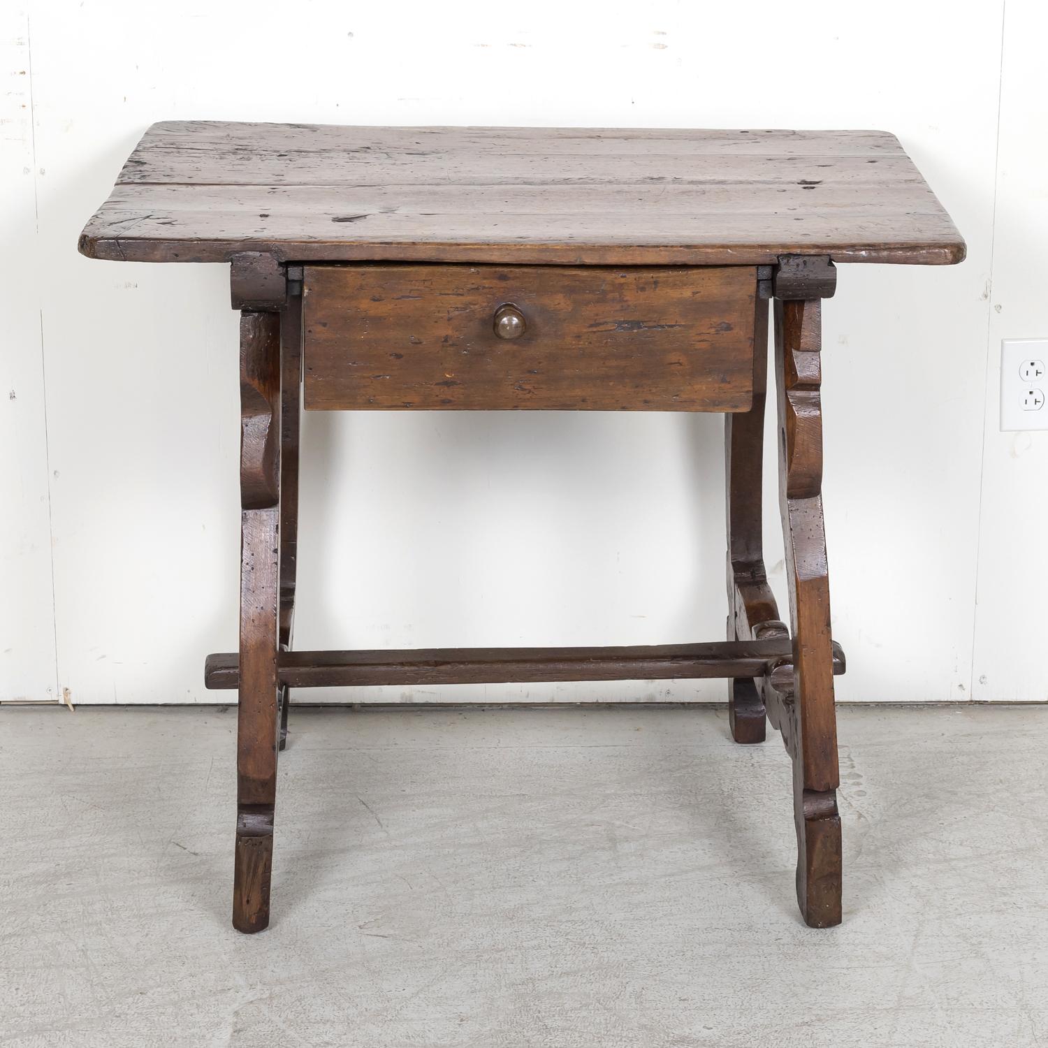A handsome 18th century Spanish side table or desk handcrafted in the late 1700s of solid walnut in the Catalan region having a rectangular plank top above a single large drawer. Raised on hand carved lyre shaped legs joined by a carved stretcher.