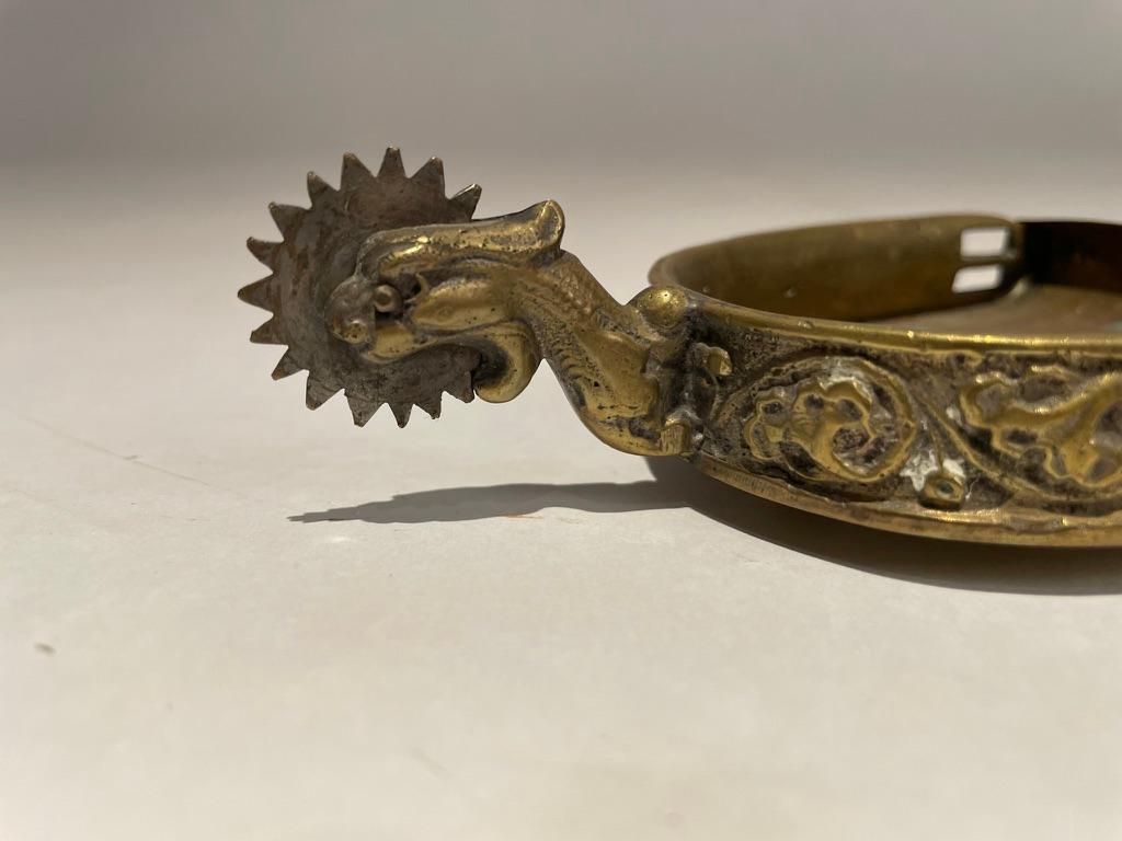 18th century Spanish Colonial bronze spur with a steel blade now made into a trinket dish or ashtray. The beautifully crafted spur with raised floral design and a fierce griffin or dragon head holding the blade. The later brass dish is beautifully