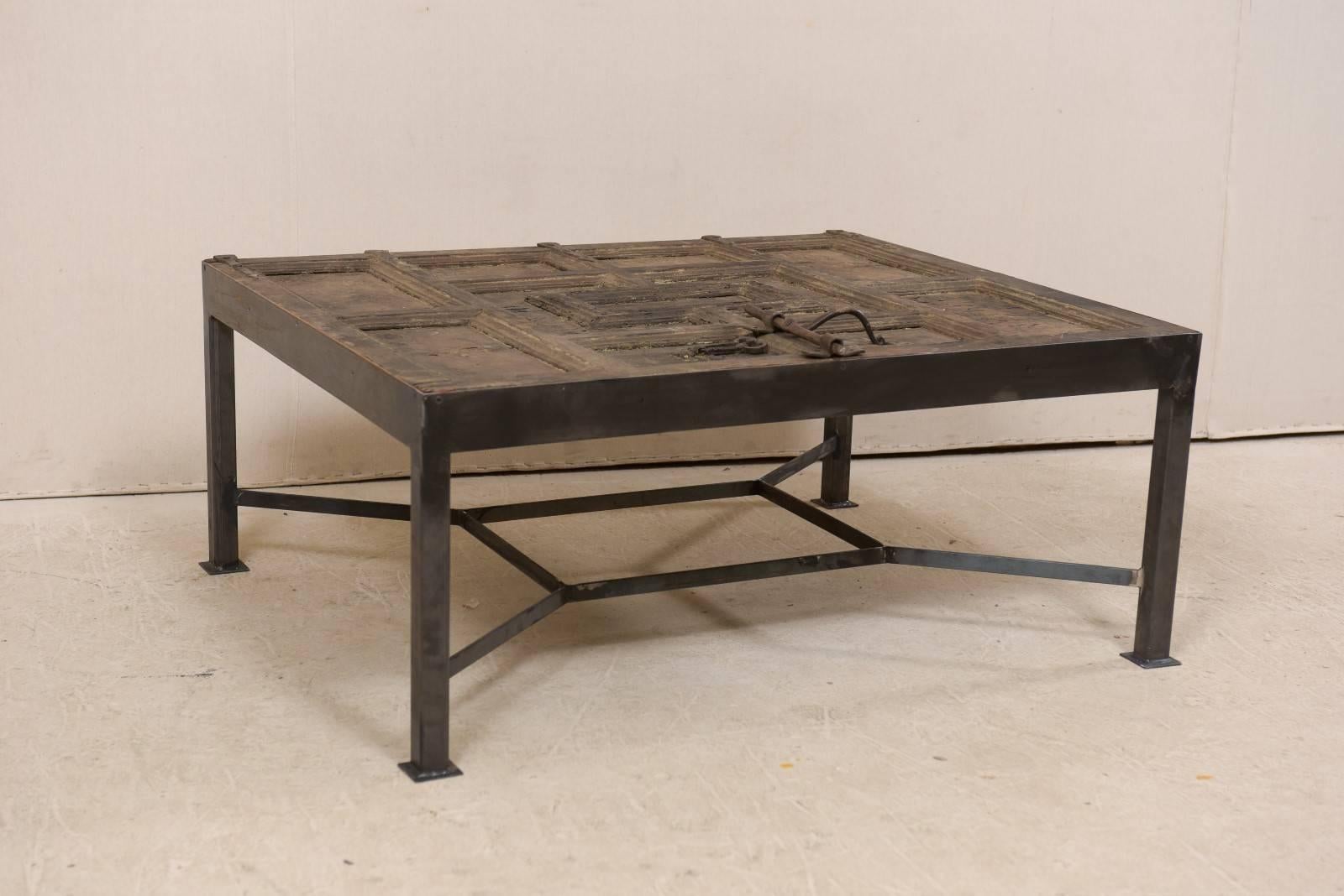 This is a custom coffee table made from an 18th century Spanish door. This wonderfully unique coffee table has been fashioned from an 18th century Spanish door, with geometrical recessed panels and it's original iron hardware and latch adorning the