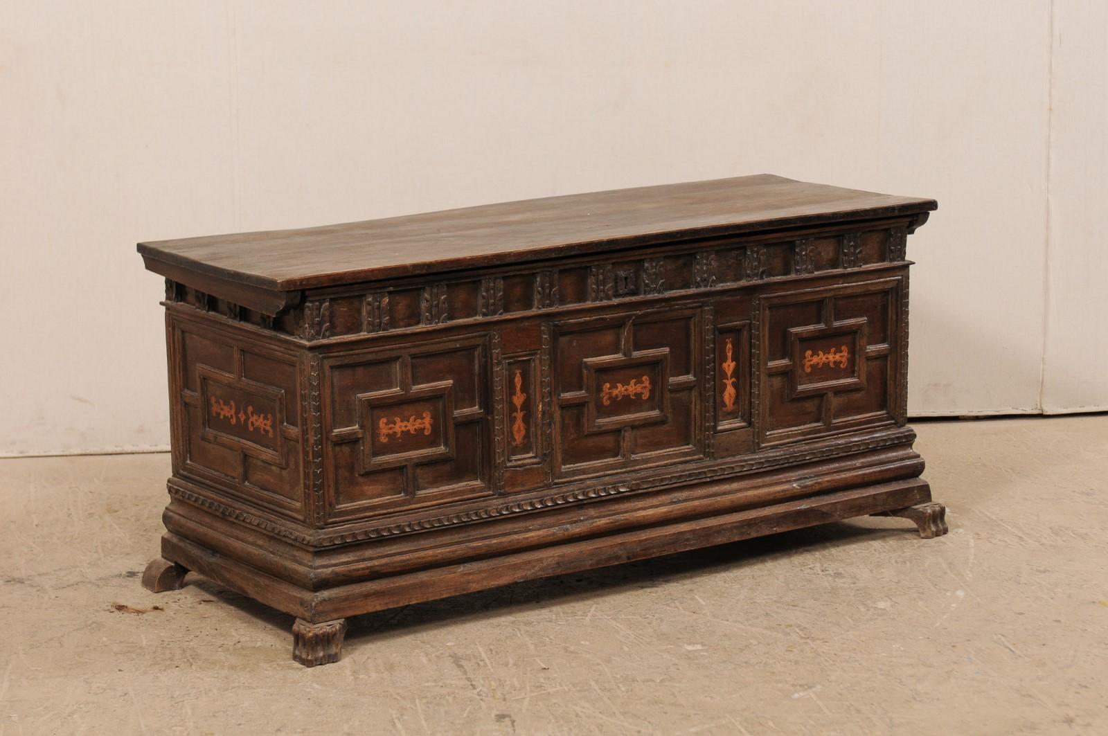 A Spanish 18th century large size carved-wood coffer. This Spanish trunk from the 18th century features a long rectangular-shaped top which rests above a beautifully carved case adorn with a leaf motif moldings and geometrically designed panels with