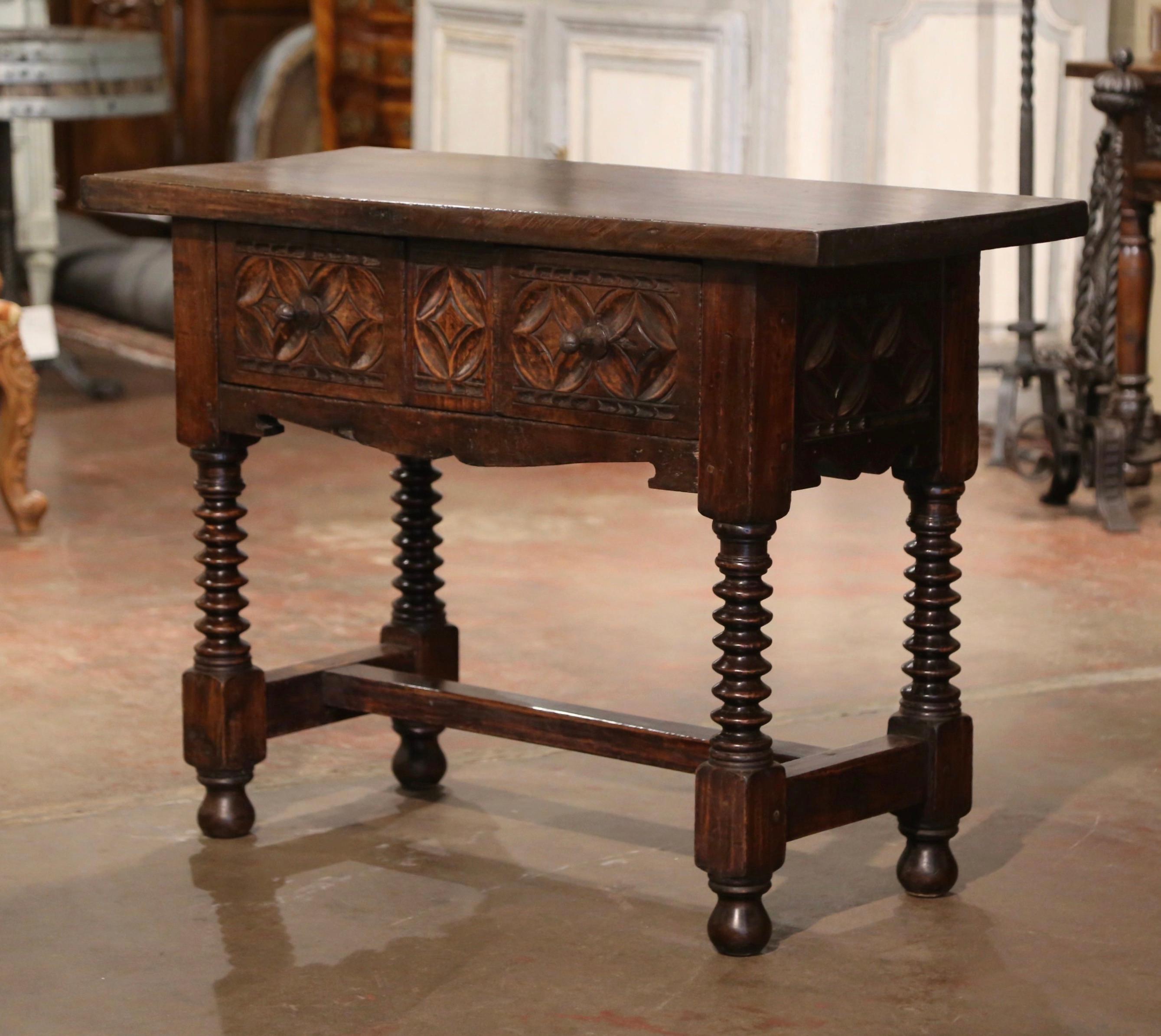 Crafted in Spain circa 1780, the antique console table stands on thick carved spool turned legs ending with bun feet, and embellished with a bottom stretcher. The tall table with scalloped apron, features two hand carved drawers across the front