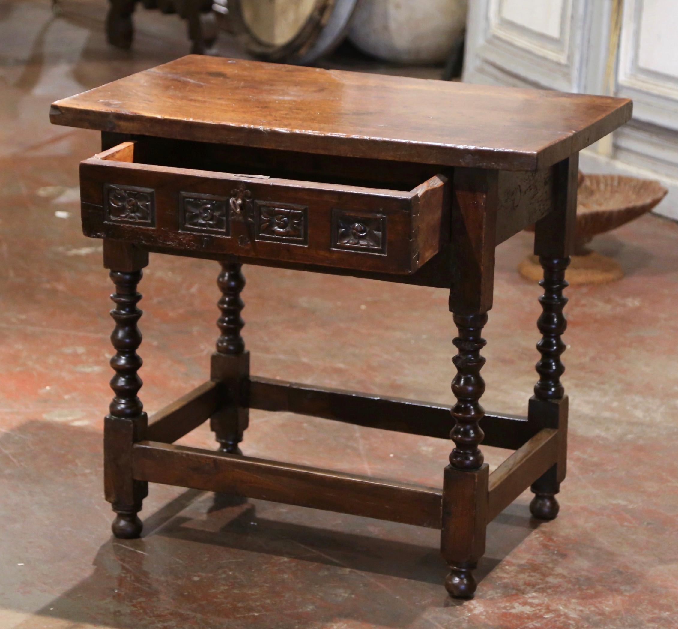 Crafted in Spain circa 1780, and built of walnut wood, the antique occasional table stands on thick carved spool turned legs ending with bun feet, and embellished with a bottom stretcher. The side table features a hand carved drawer across the front