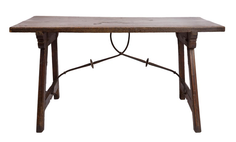 This 18th century Spanish trestle style writing table has a tabletop of one single wide plank, and the leg sections, or trestles, are joined with sliding dovetail joints and fastened in place with wrought iron stretchers. Both trestles are hinged at