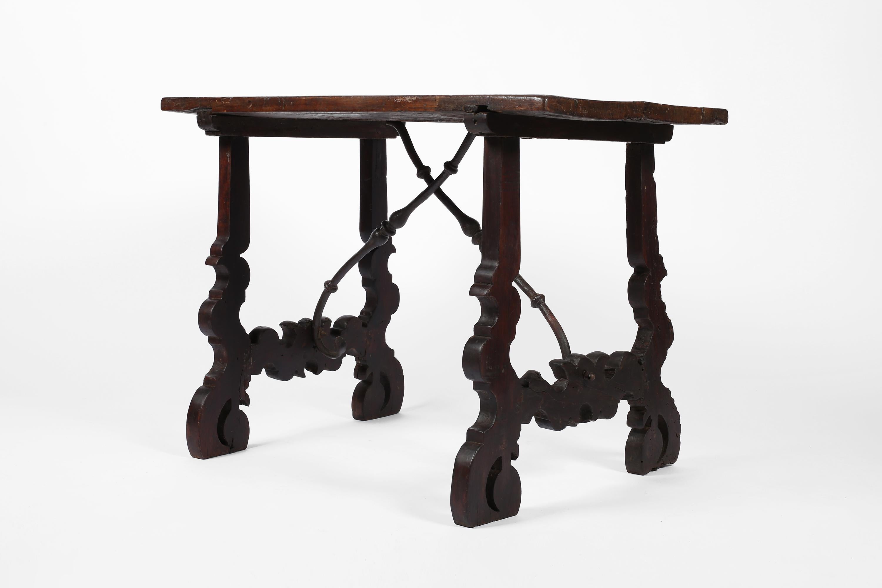 A charming 18th century side table, console or small desk in heavily patinated walnut timber. The characterful single plank top sitting on traditional decoratively carved legs, with forged iron stretchers. Spanish, c. 1750.