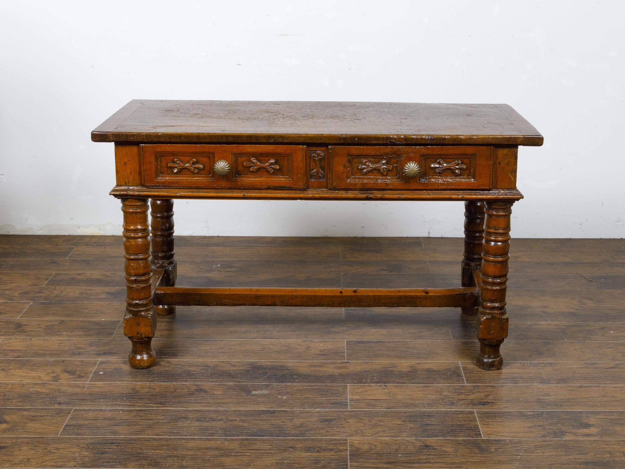 A Spanish walnut console table from the 18th century with two carved drawers, turned baluster legs and H-Form cross stretcher. This 18th-century Spanish walnut console table marries historical charm with exquisite craftsmanship. The table features