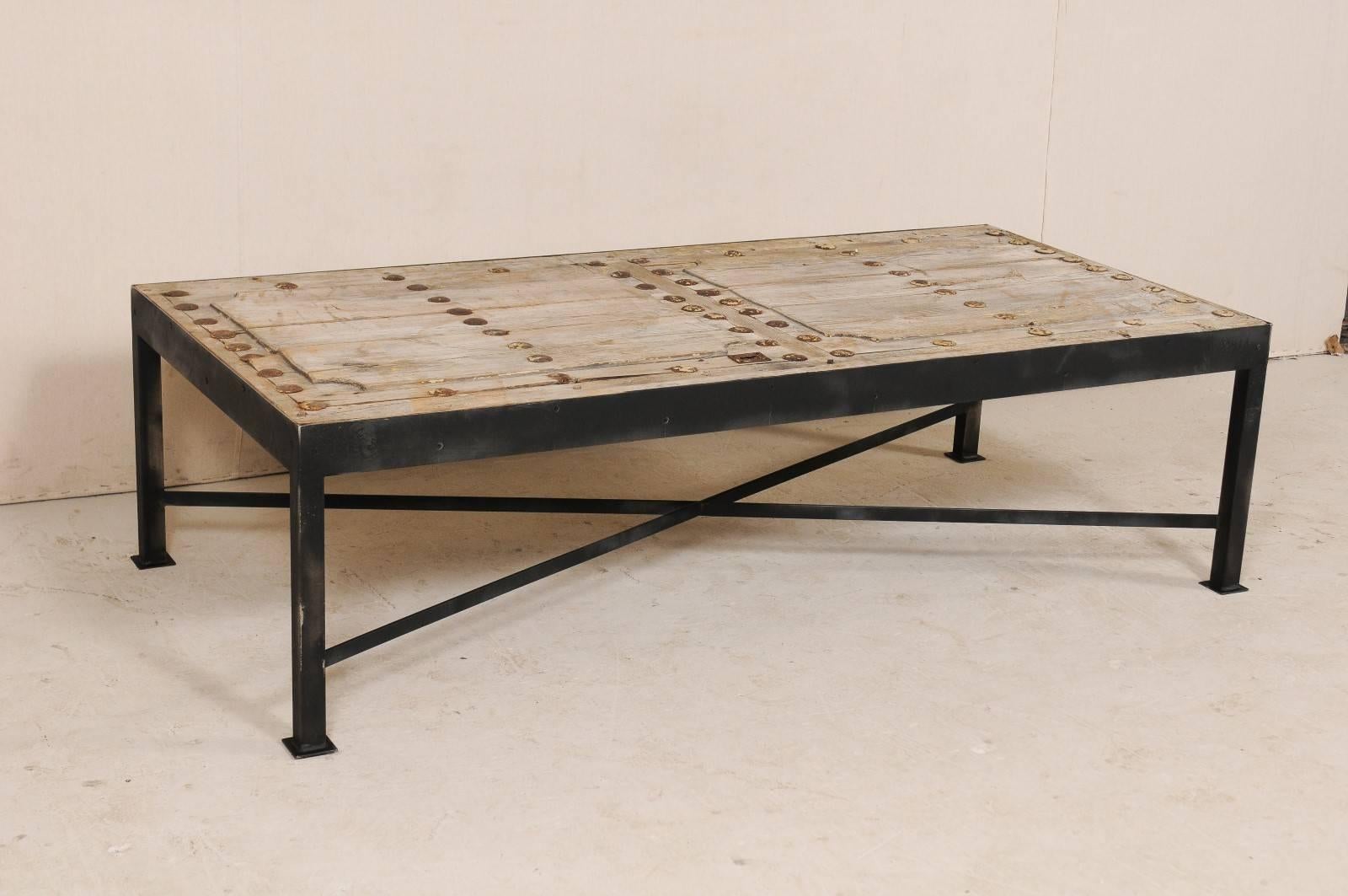 This is a custom coffee table made from an 18th century Spanish door. This unique coffee table has been fashioned from an 18th century Spanish door, with it's wonderful old patina and original round iron grommets and escutcheon hardware, set onto a