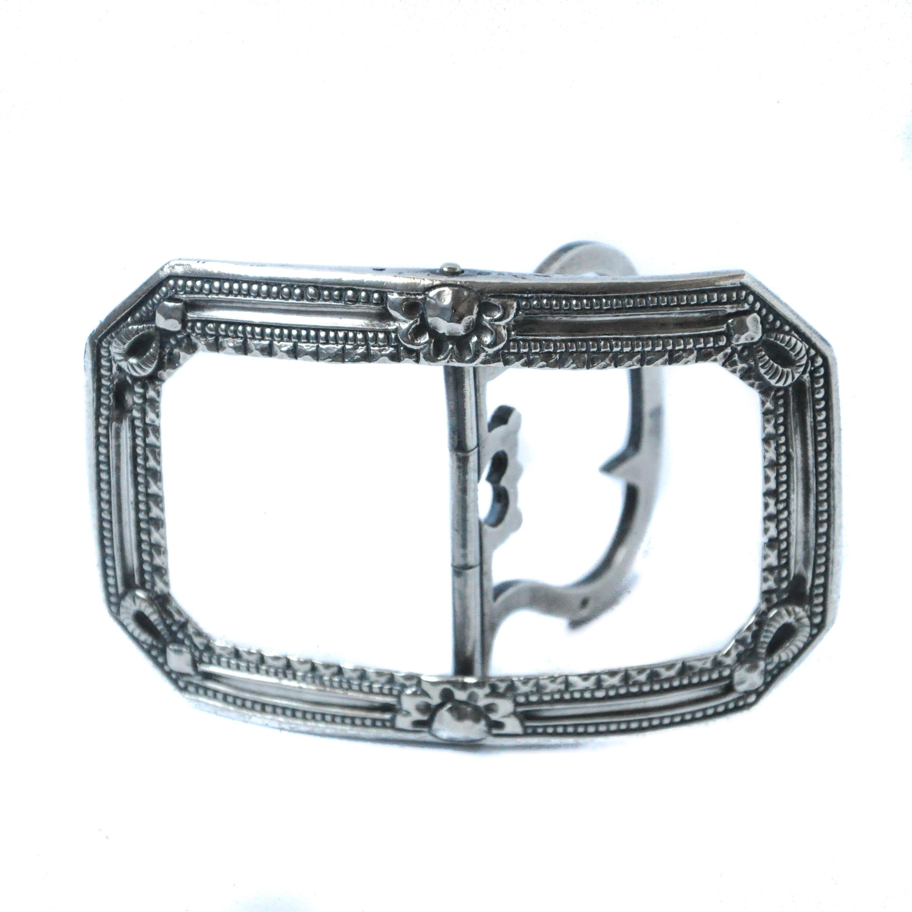 This silver rectangular curved sash buckle is made in early nineteenth century, Georgian era. The central pillar is hinged with a two-prong, which is flanked by an openwork heart-shaped motif. Furthermore, two rosettes and fantasy motifs are etched