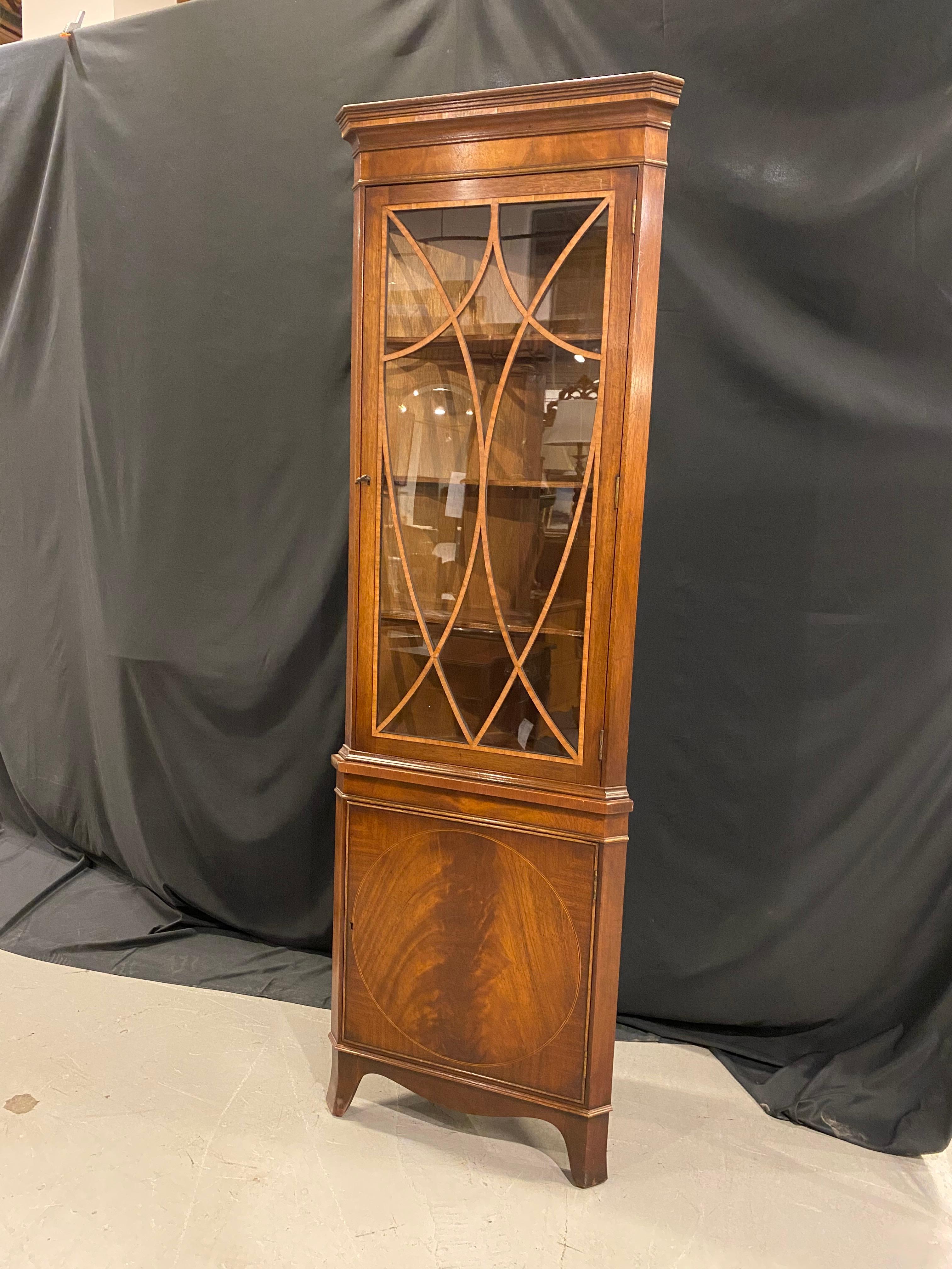 This is a beautifully balanced 18th century style corner cabinet crafted in mahogany with a lovely satin wood banded fret work detail, in the Sheraton style, on the upper door which hold individually hand glazed glass panels. The lower door is a