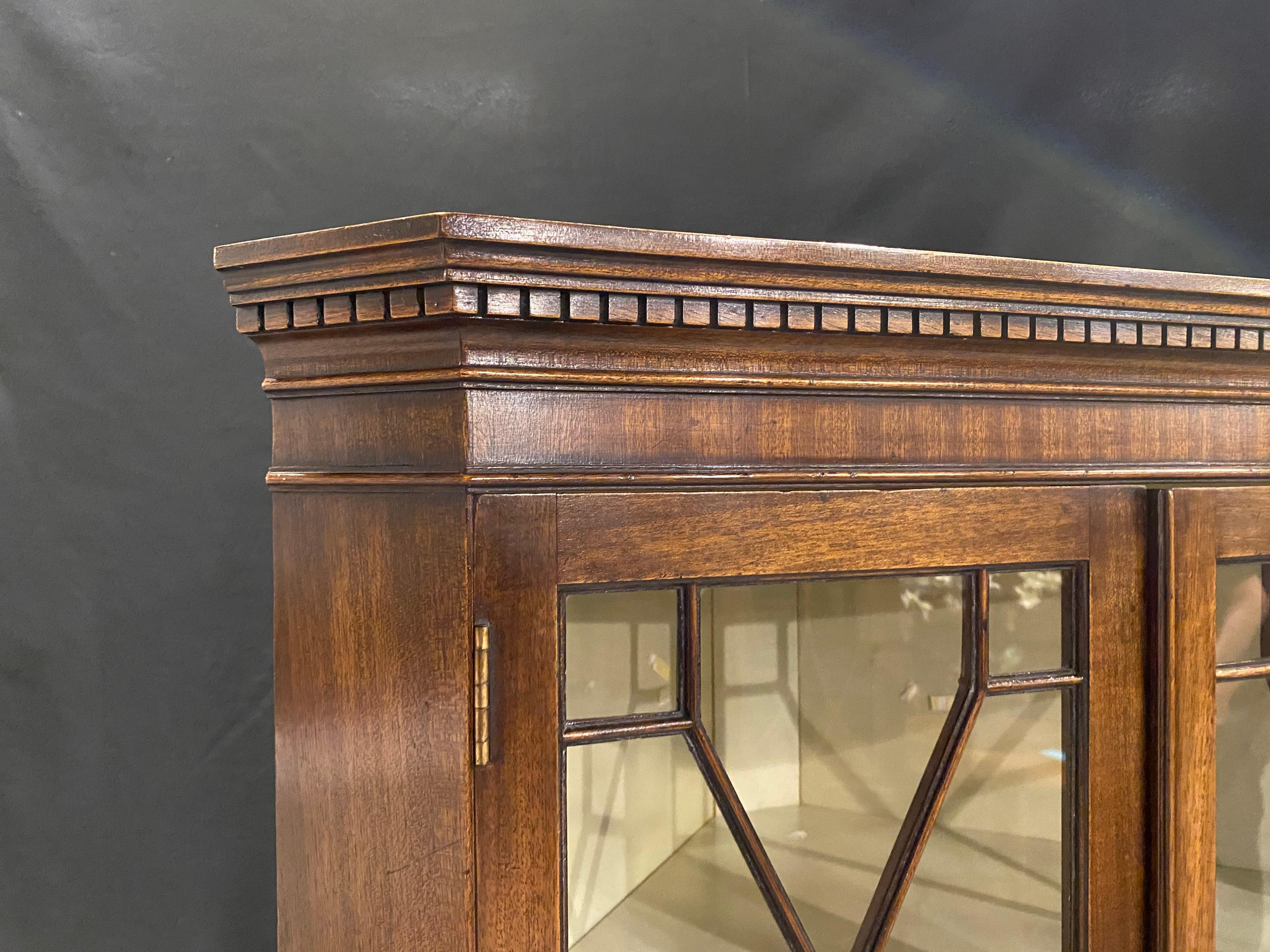 This is a lovely mahogany corner cabinet in the 18th century Georgian styling. The top has two glass doors with 13 panels of hand glazed glass panels in each door. Behind which is a cream finish interior that lightens the interior to contrast the