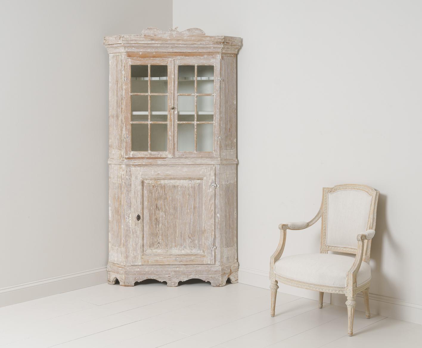 A late Baroque period corner vitrine cabinet from the 18th century in hand-scraped original paint with scalloped base and reeded sides and door. Original lock with key. Original glass. The upper section contains two shelves, the top shaped and